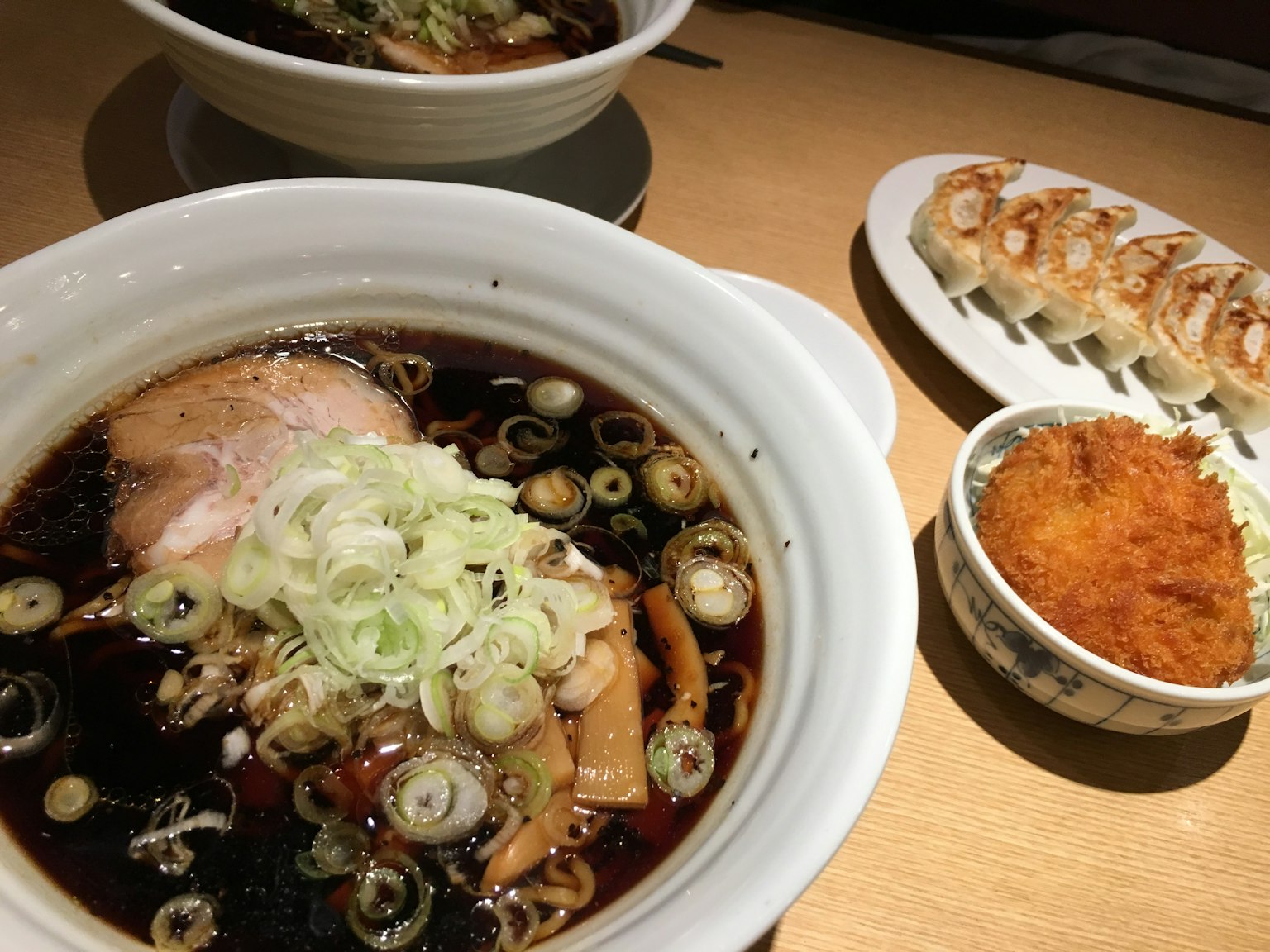 Bowl of ramen topped with green onions and sliced pork alongside a plate of fried food and grilled dumplings