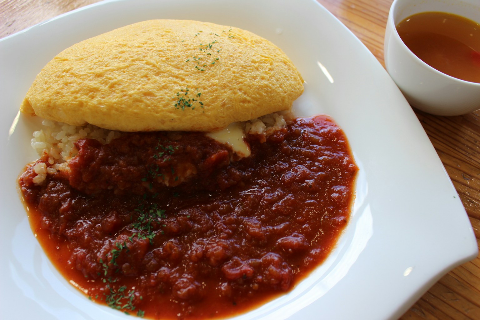 Teller mit Omurice und Tomatensauce sowie einer Tasse Suppe