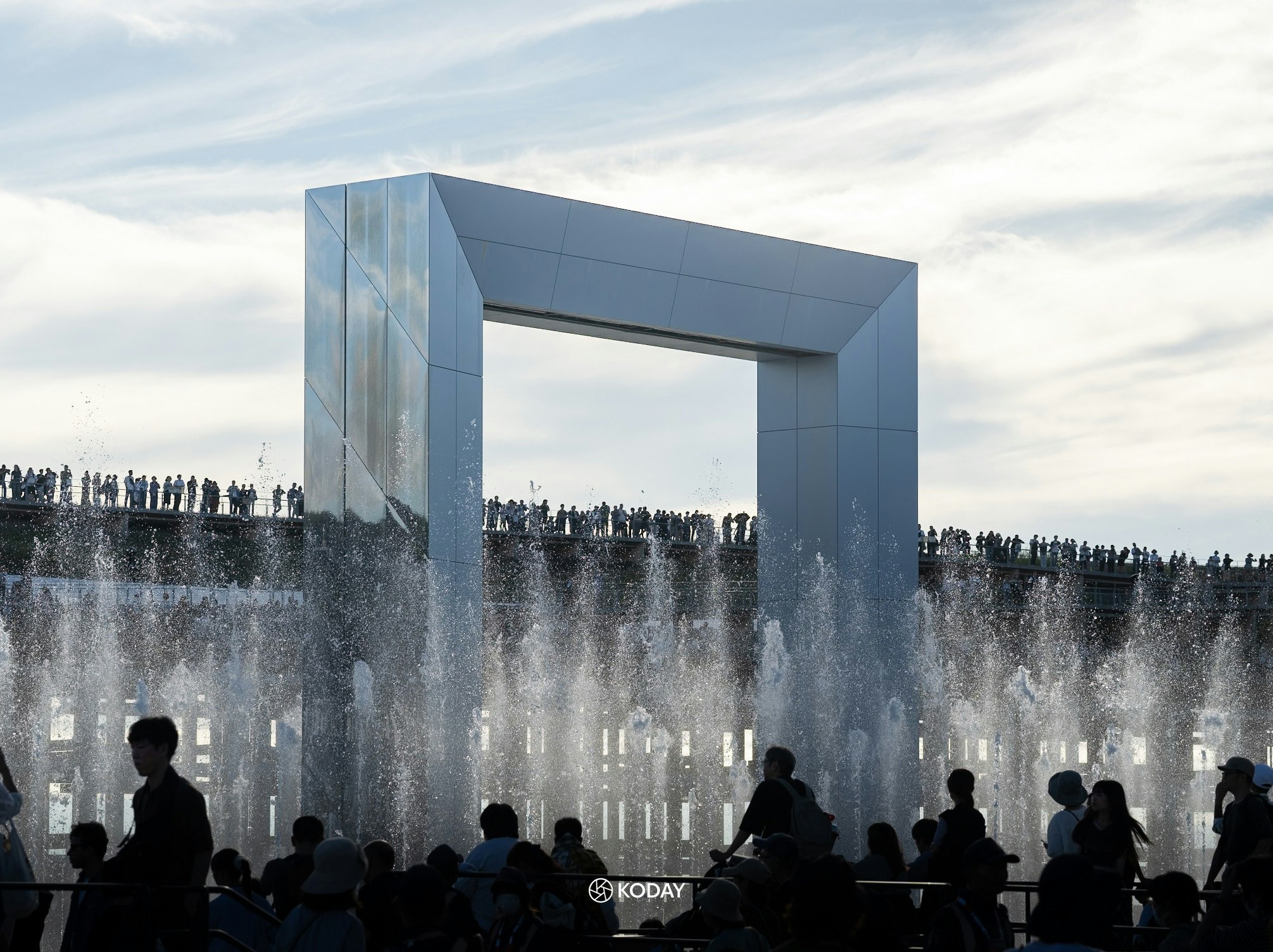 escena del final de la Expo de Osaka con cortina de agua de una fuente y visitantes en silueta frente a la entrada