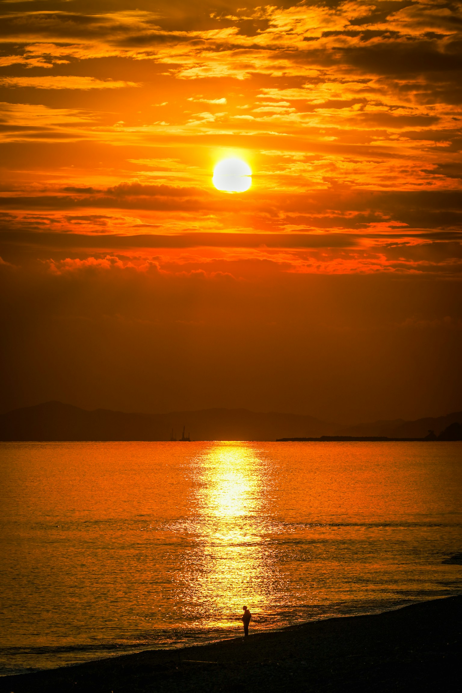 Scenic view of sunset over the ocean with a lone figure on the beach