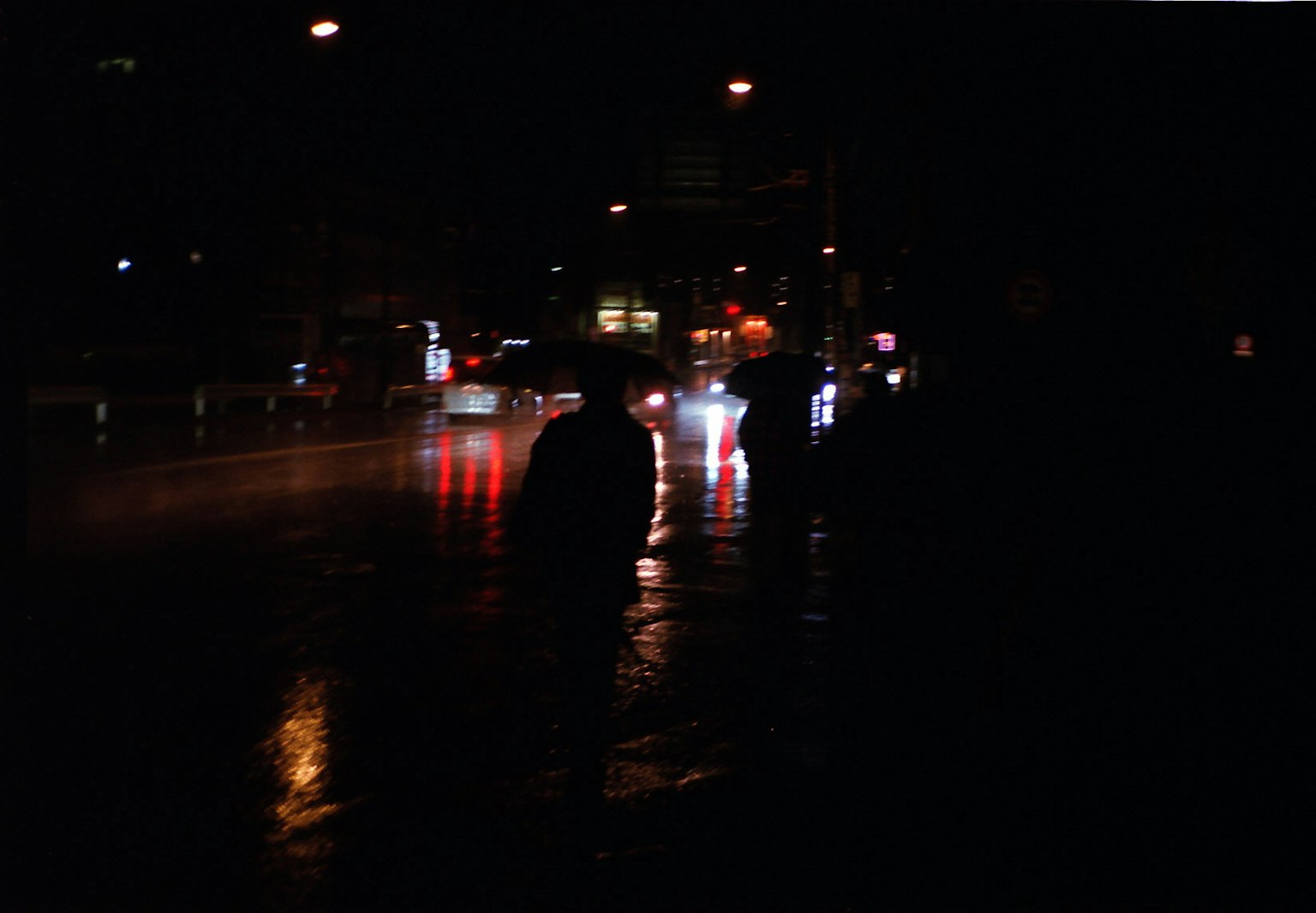 Silhouette di persone a un angolo di strada buio con luci di auto