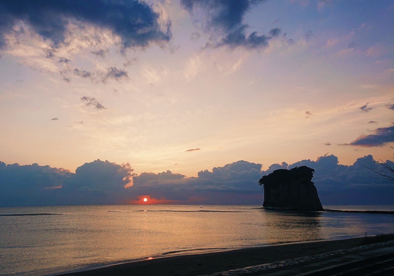 Beach scene with sunset over the sea and clouds in the sky