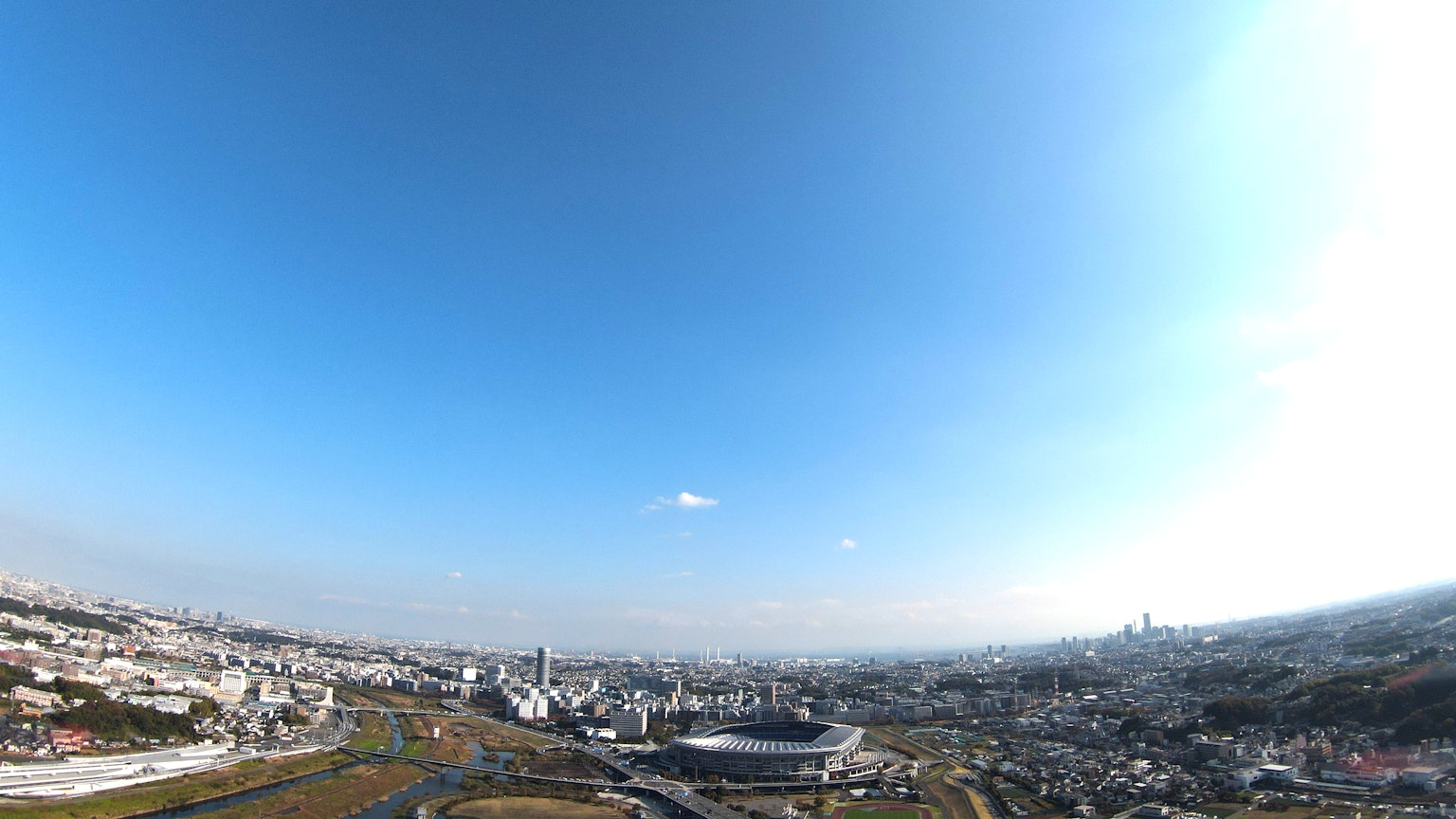 Pemandangan panorama kota di bawah langit biru cerah dengan stadion dan gedung pencakar langit terlihat