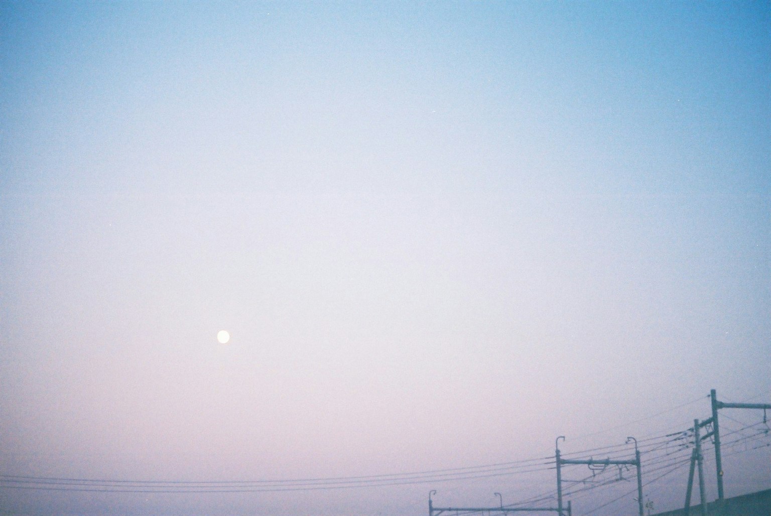 Cielo blu e rosa chiaro con una luna visibile e linee elettriche