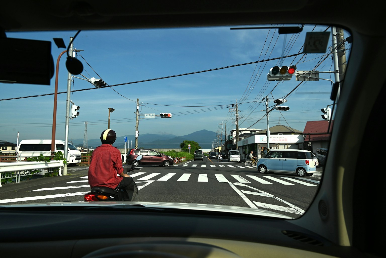 从车窗外看，显示交通信号和人行横道，背景有一座山