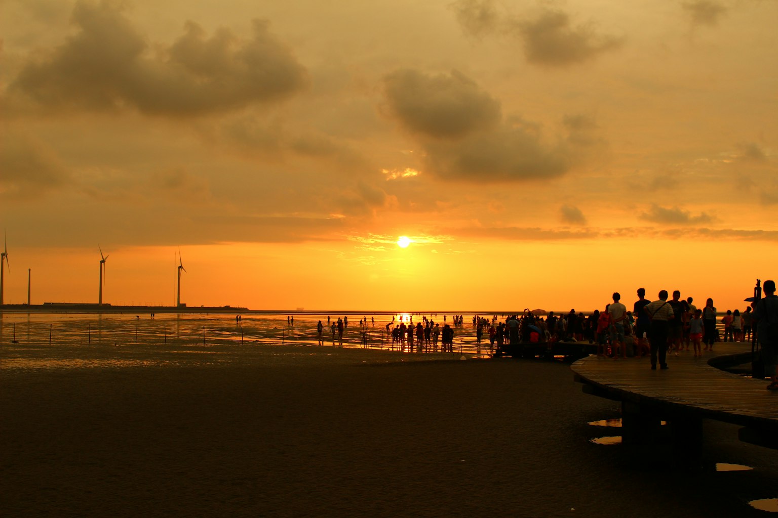 Silhouette di persone su una spiaggia al tramonto con turbine eoliche