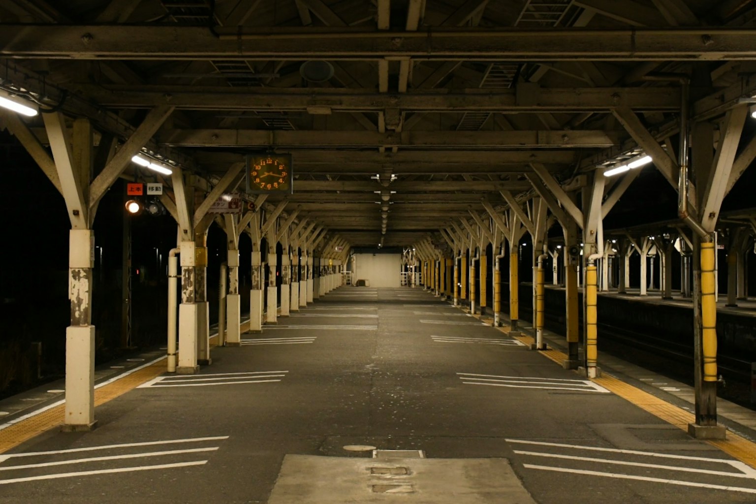 Plateforme de train calme avec des piliers en bois et des lumières la nuit
