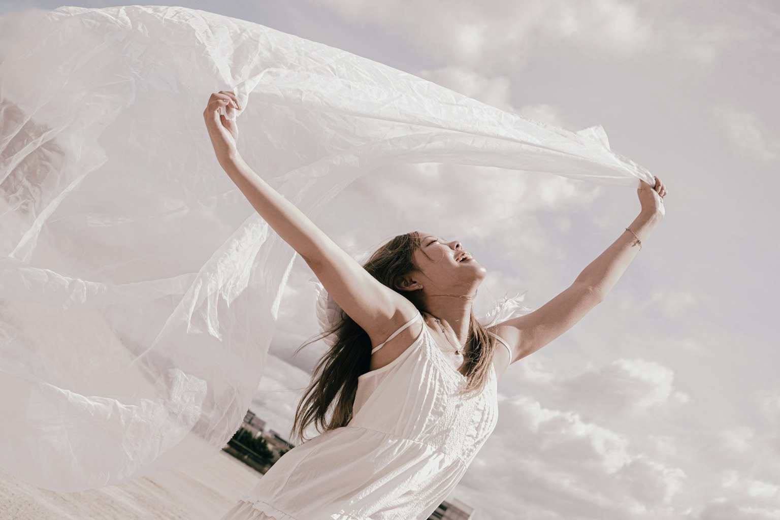 白い布を持ち上げて喜ぶ女性の姿 青空と雲の背景