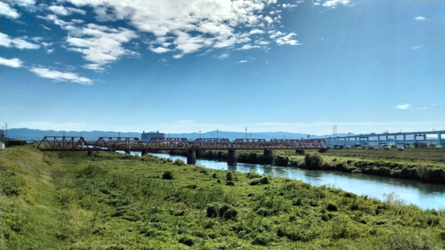 Pemandangan indah padang rumput hijau dan sungai di bawah langit biru dengan jembatan di kejauhan
