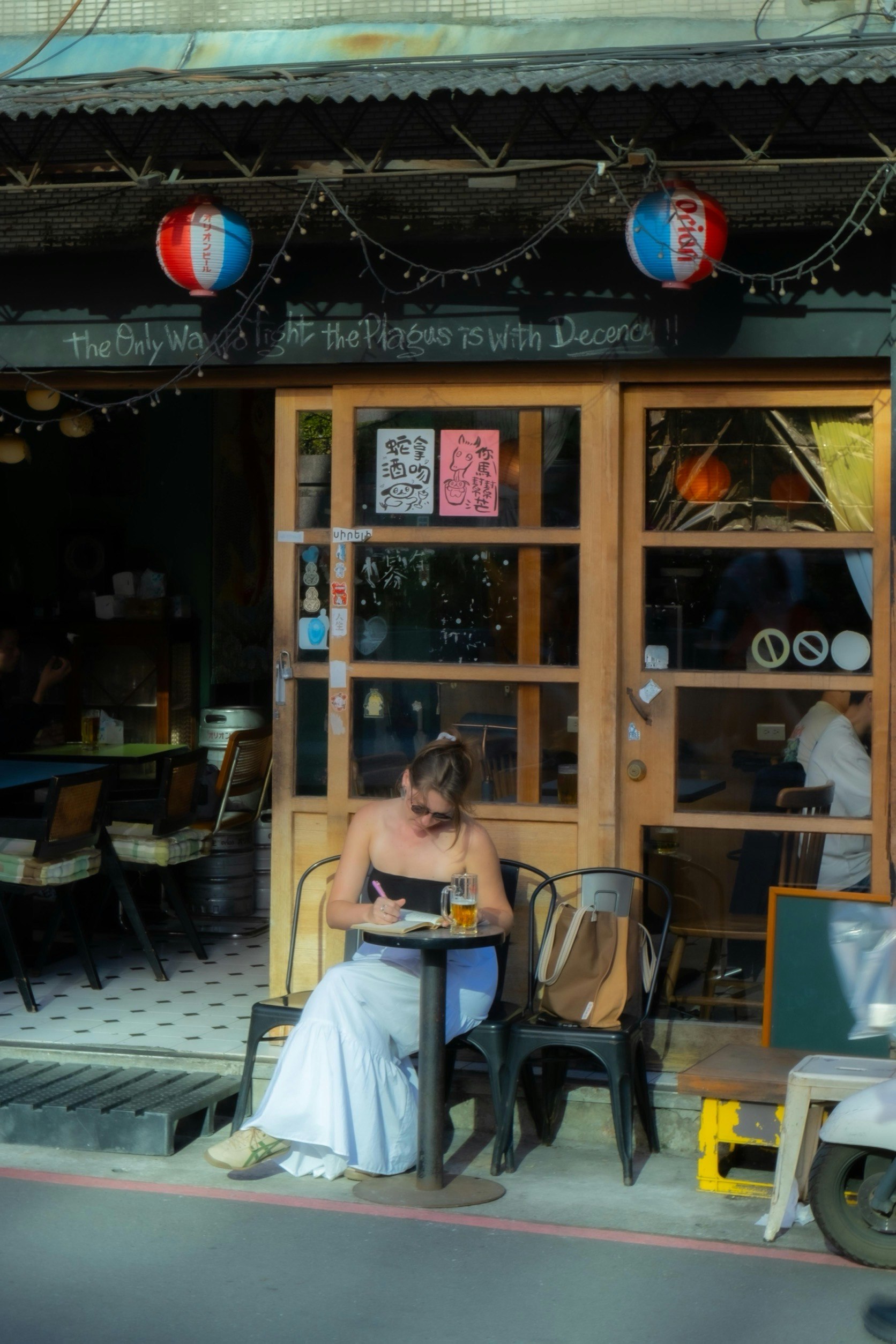 Una donna legge con una birra davanti a un’izakaya giapponese in via Cefeng a Taipei
