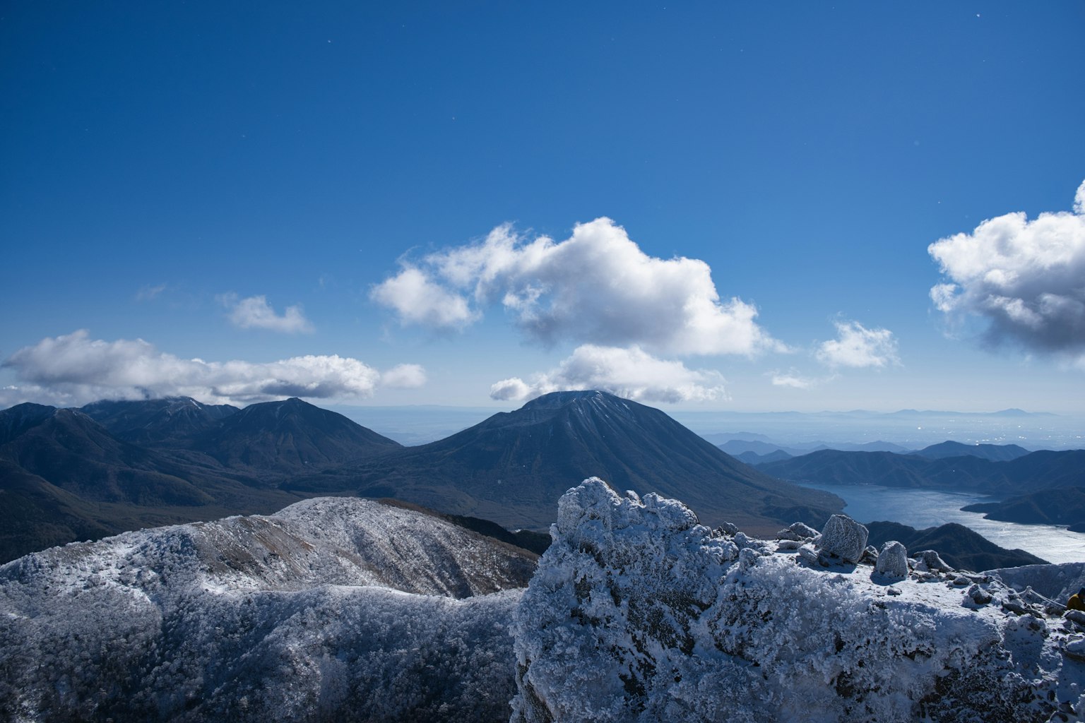 Vista panoramica dalla cima innevata di una montagna con cielo blu e nuvole bianche e silhouette di un vulcano in lontananza