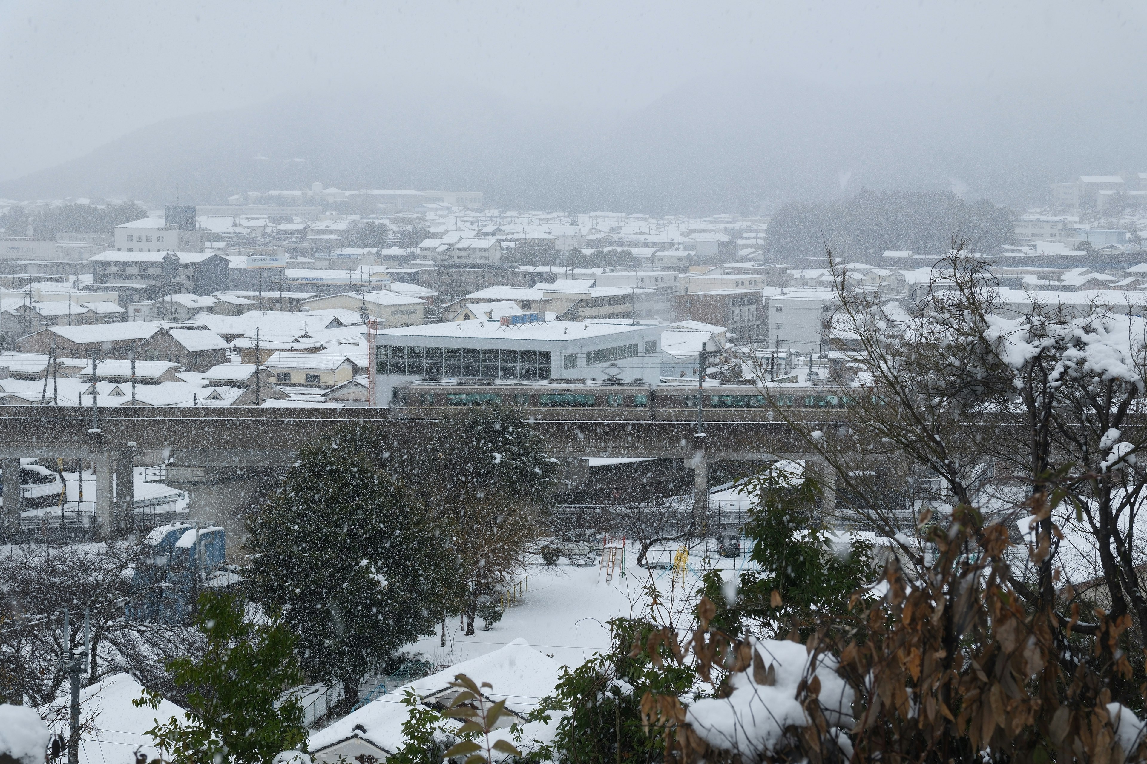 雪の降る福知山市の街並みと山陰本線の電車