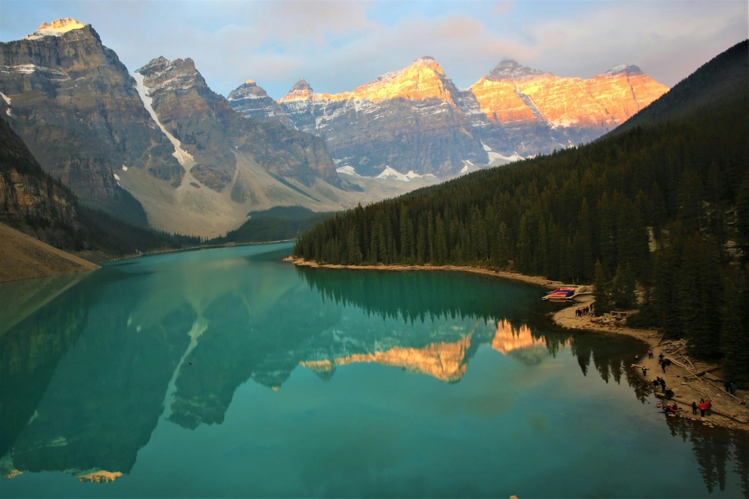 Vista panoramica di un lago turchese che riflette le montagne circostanti all'alba