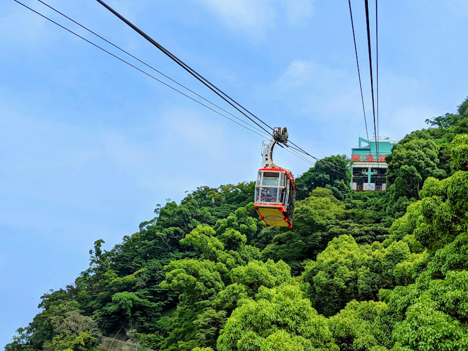 A cable car moving through lush green mountains under a blue sky