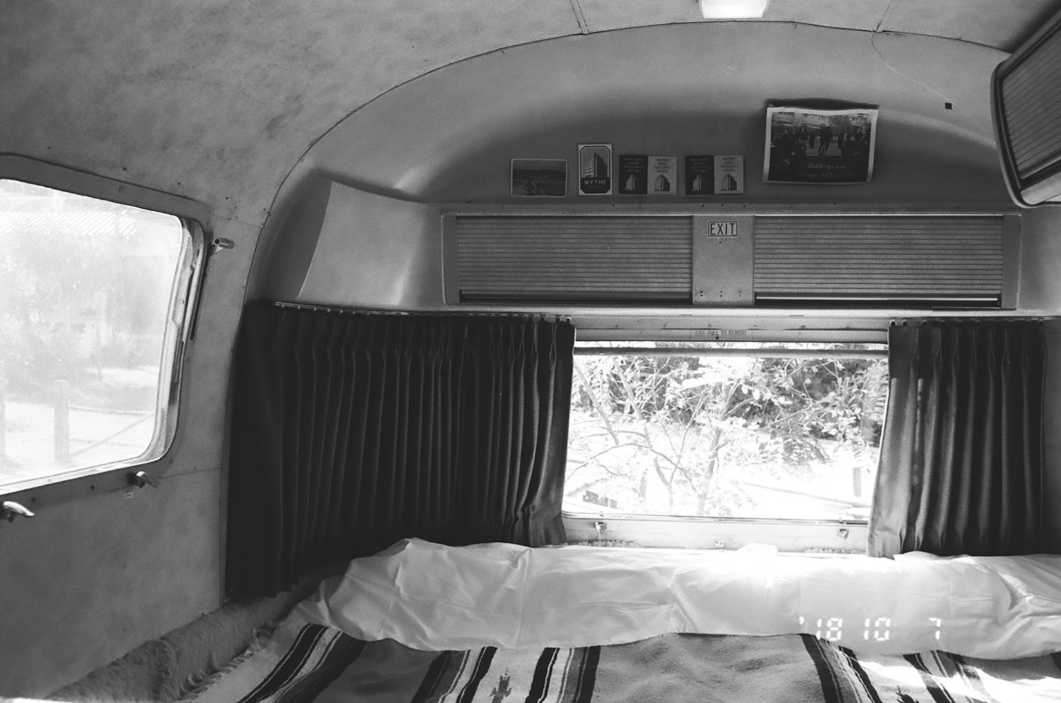 Innenansicht eines vintage Wohnwagens in Schwarzweiß mit einem Fenster und Vorhängen und einem Bett