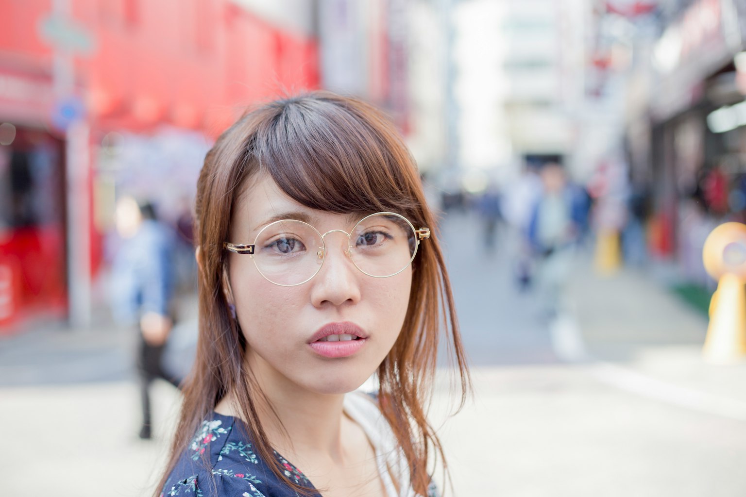 Portrait d'une femme regardant la caméra dans une rue animée avec des gens et des bâtiments rouges en arrière-plan