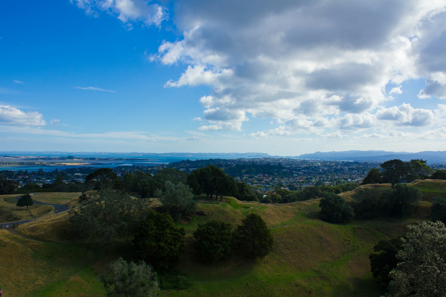 Vue panoramique depuis une colline avec des champs verts et des arbres sous un ciel bleu avec des nuages