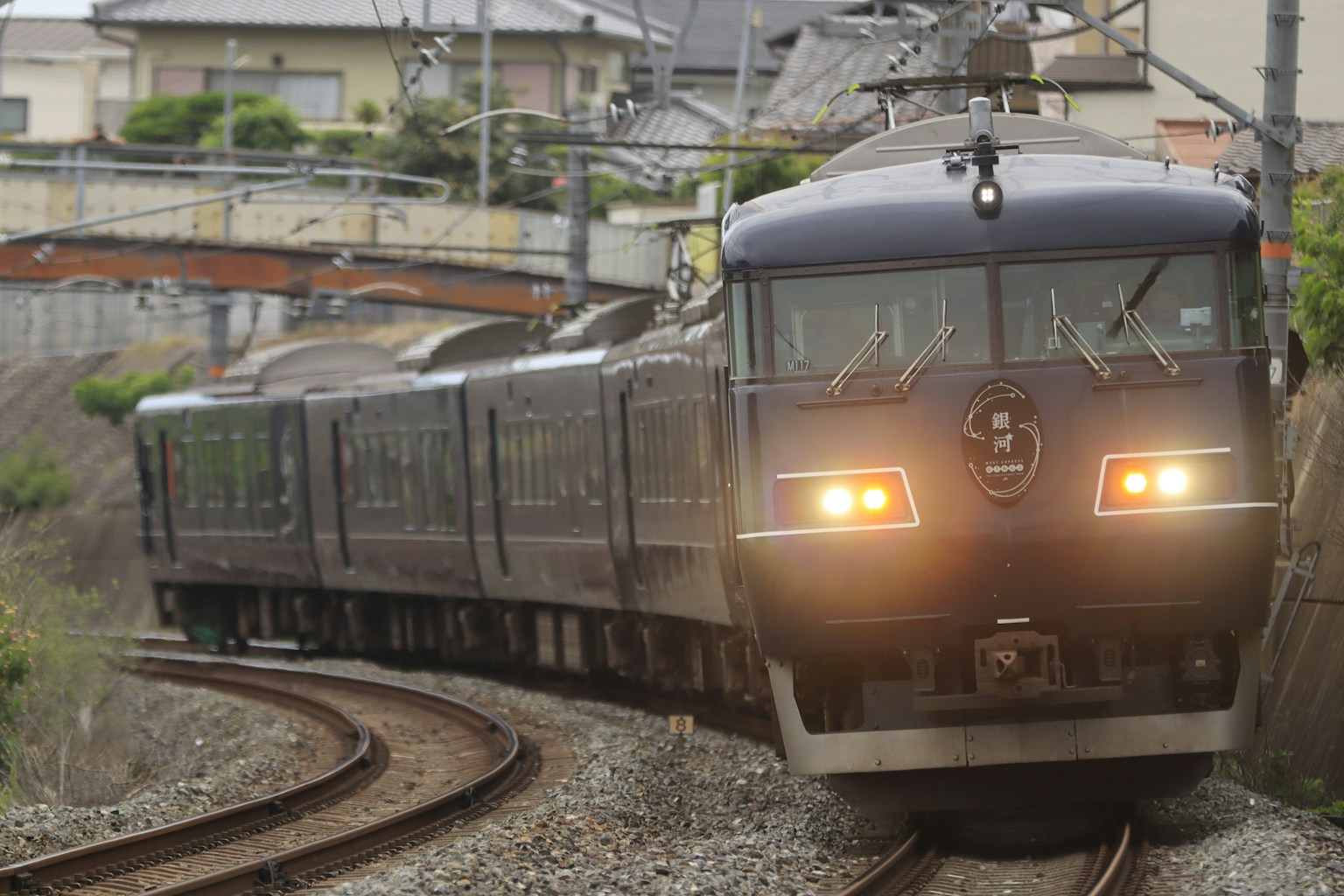 A black train navigating a curve with houses in the background