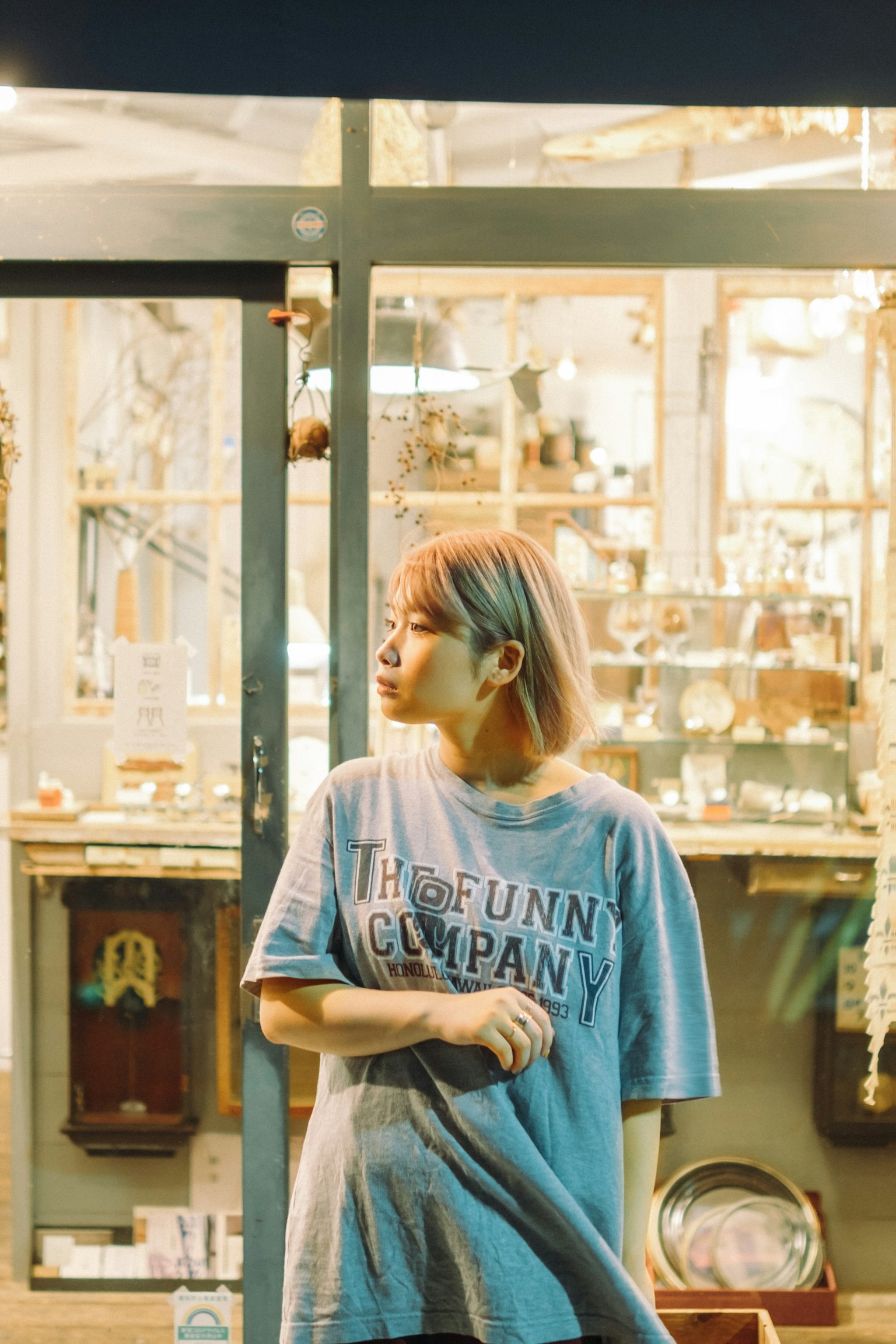 파란 티셔츠를 입은 여성이 밤에 가게 앞에 서 있다