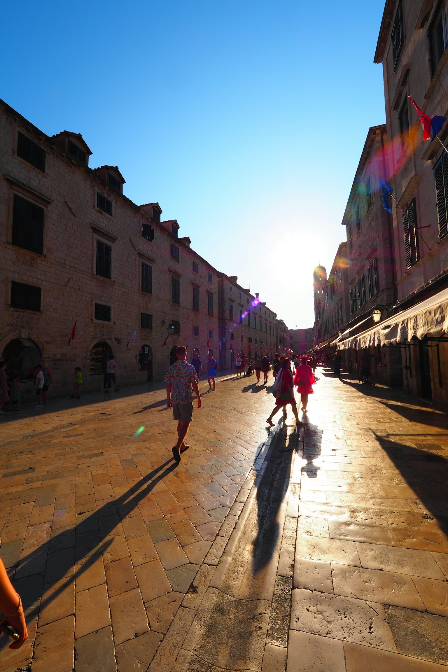 Siluetas de personas caminando por una calle iluminada por el sol con edificios a los lados