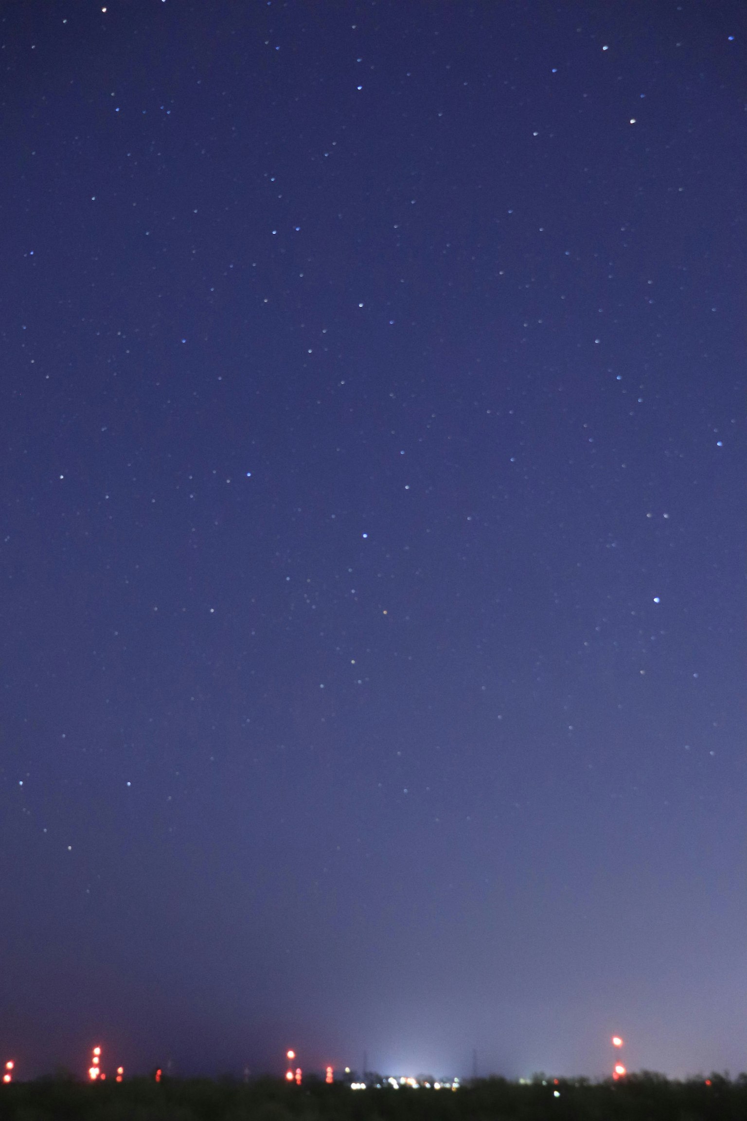 Cielo nocturno lleno de estrellas y luces rojas distantes de torres