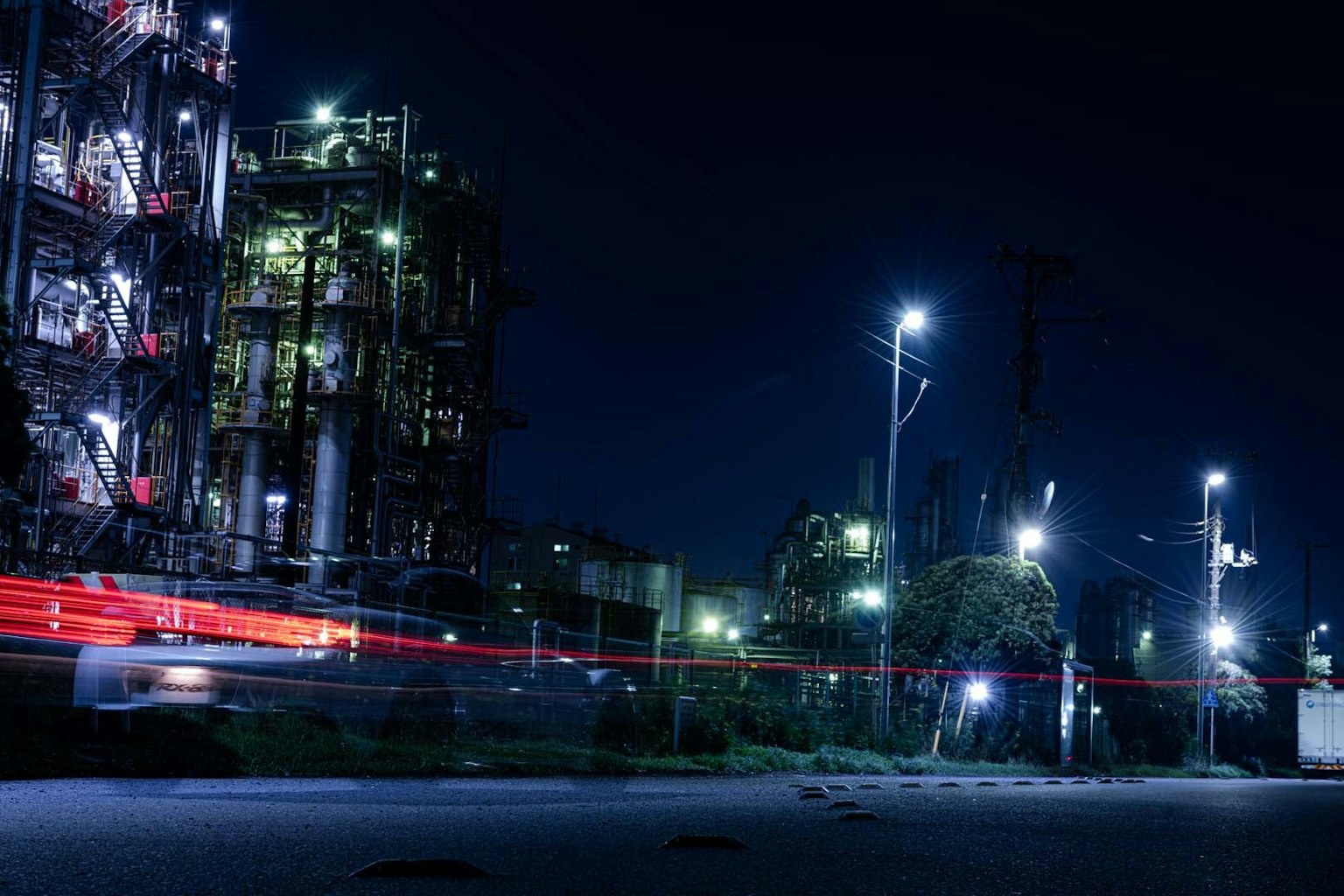 Nighttime view of a factory illuminated by lights with a passing vehicle