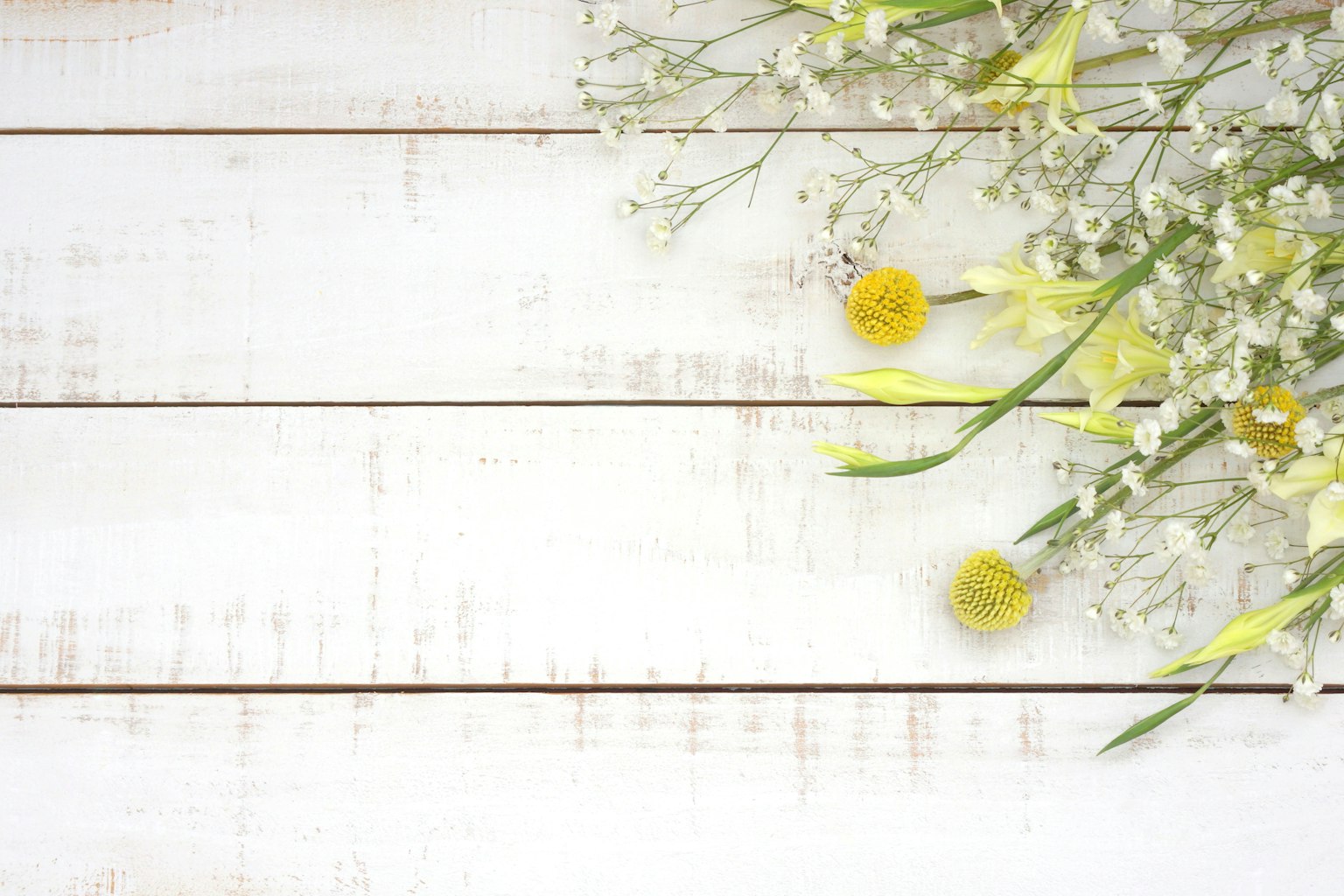 Arrangement de fleurs jaunes et de plantes vertes sur une table en bois blanc