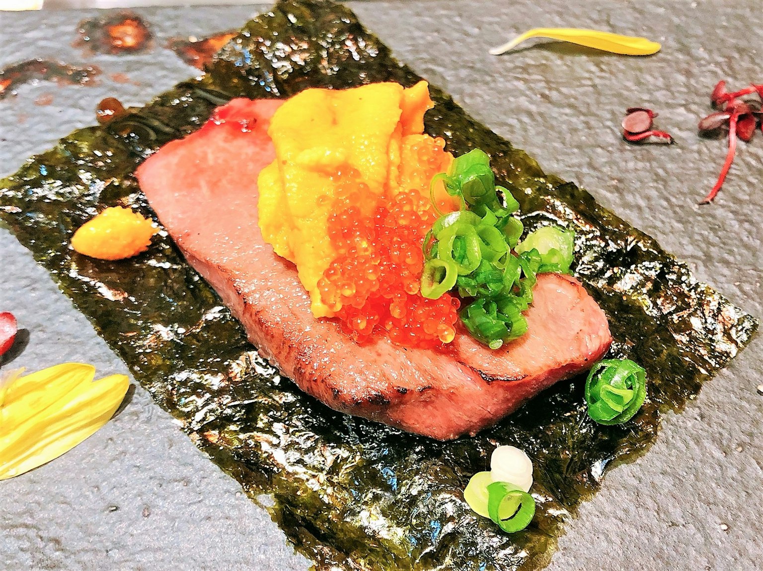 Plato de carne delicioso sobre alga con erizo de mar huevas de salmón y cebollino