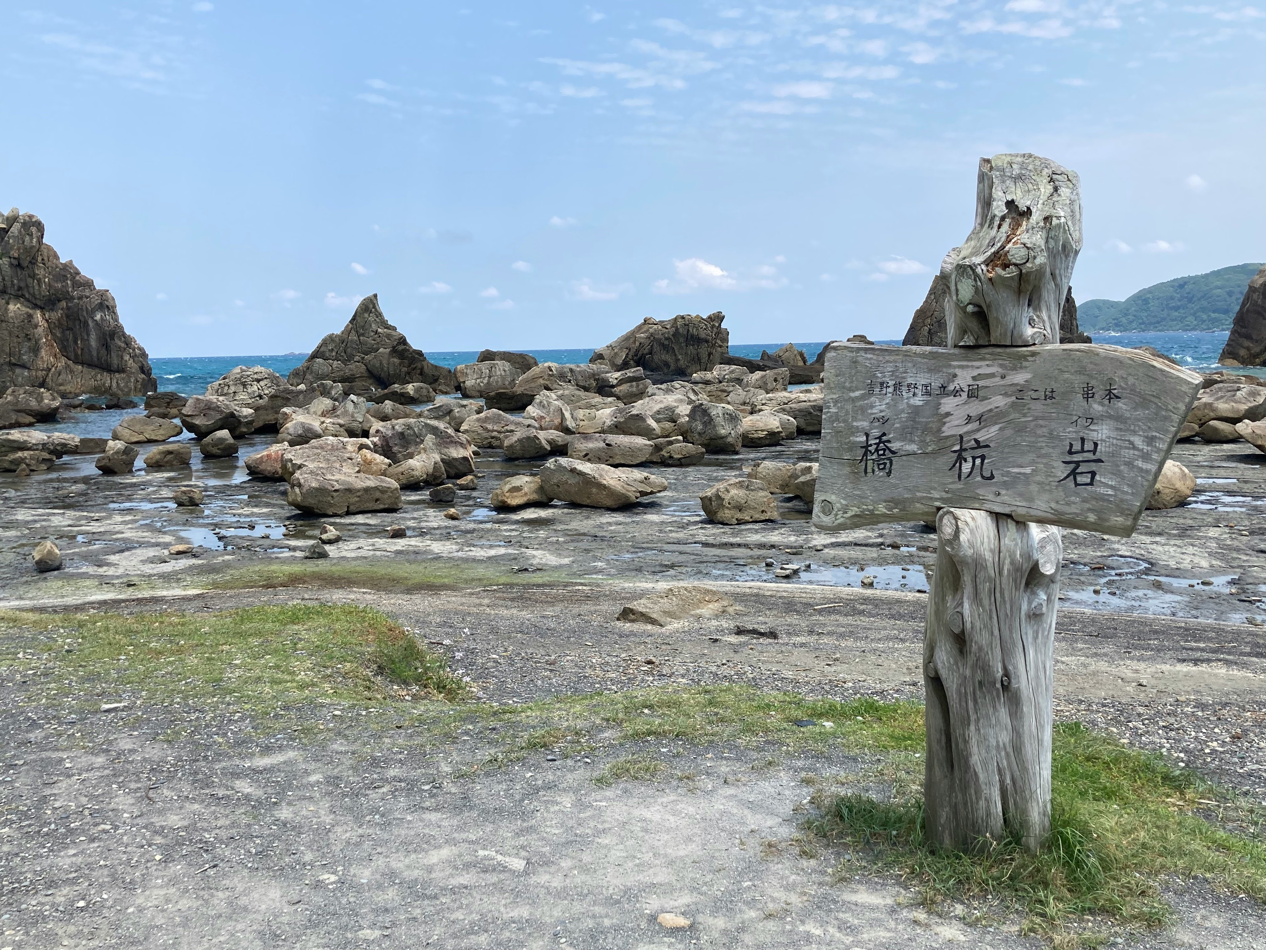 海辺の岩場と「橋杭岩」案内標柱のある景観