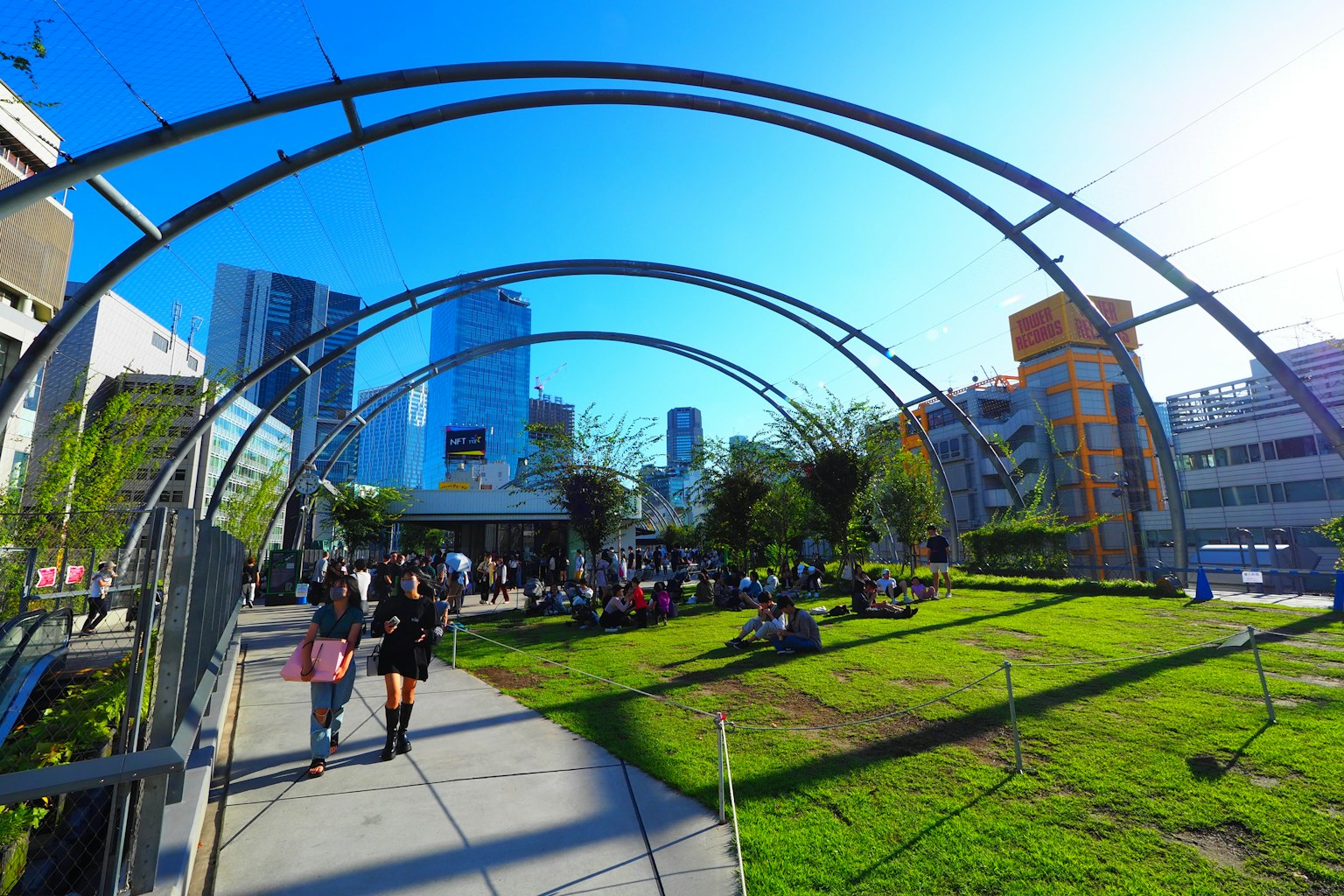 Des gens se promenant dans un parc sous un ciel bleu clair avec des bâtiments modernes