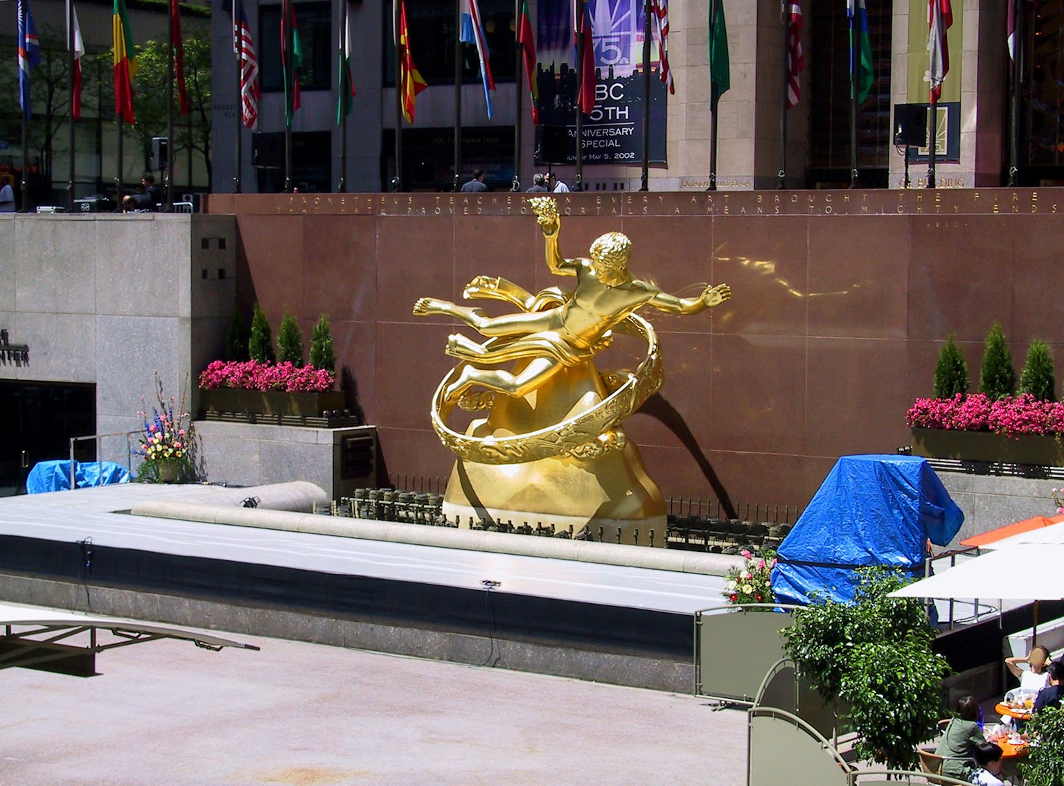 Sculpture dorée au Rockefeller Center entourée de fleurs et de drapeaux