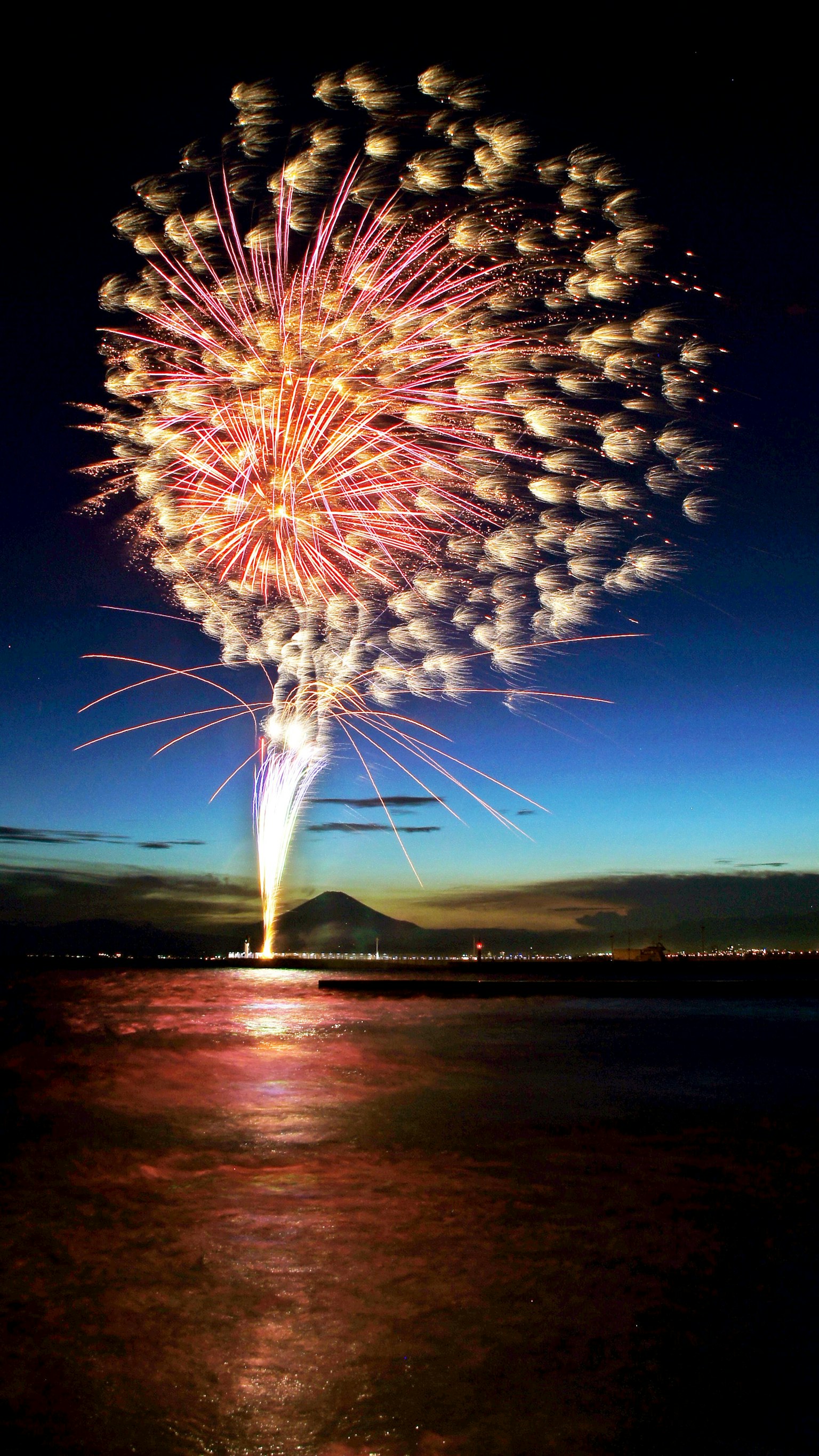 Fuochi d'artificio colorati che esplodono nel cielo notturno riflettendosi sulla superficie dell'acqua