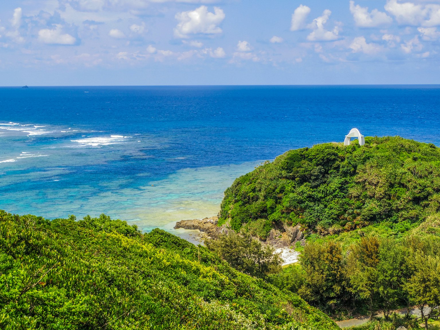 Pemandangan indah laut biru dan bukit hijau dengan struktur putih kecil