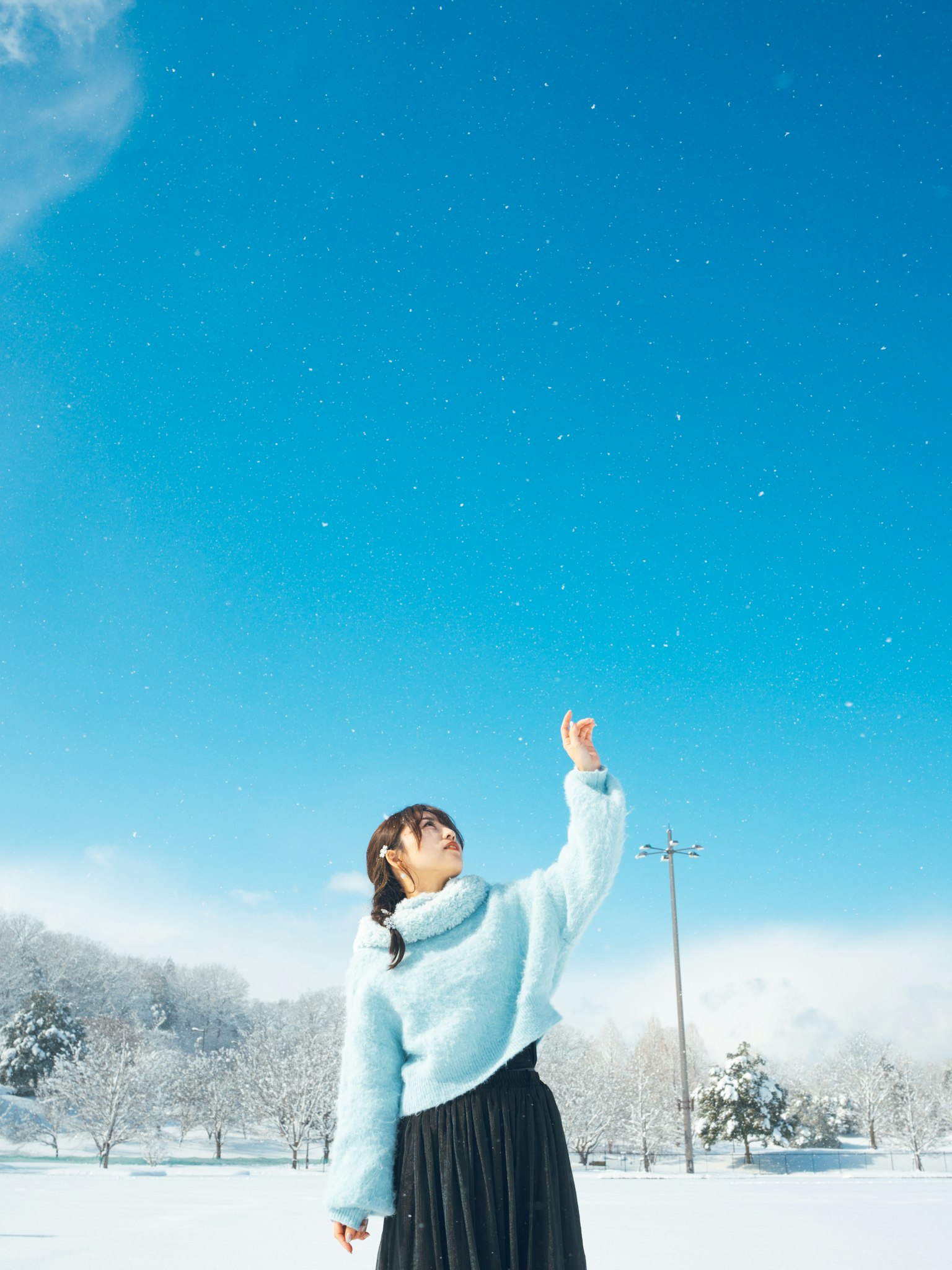 A woman in a blue sweater reaching up in a snowy landscape