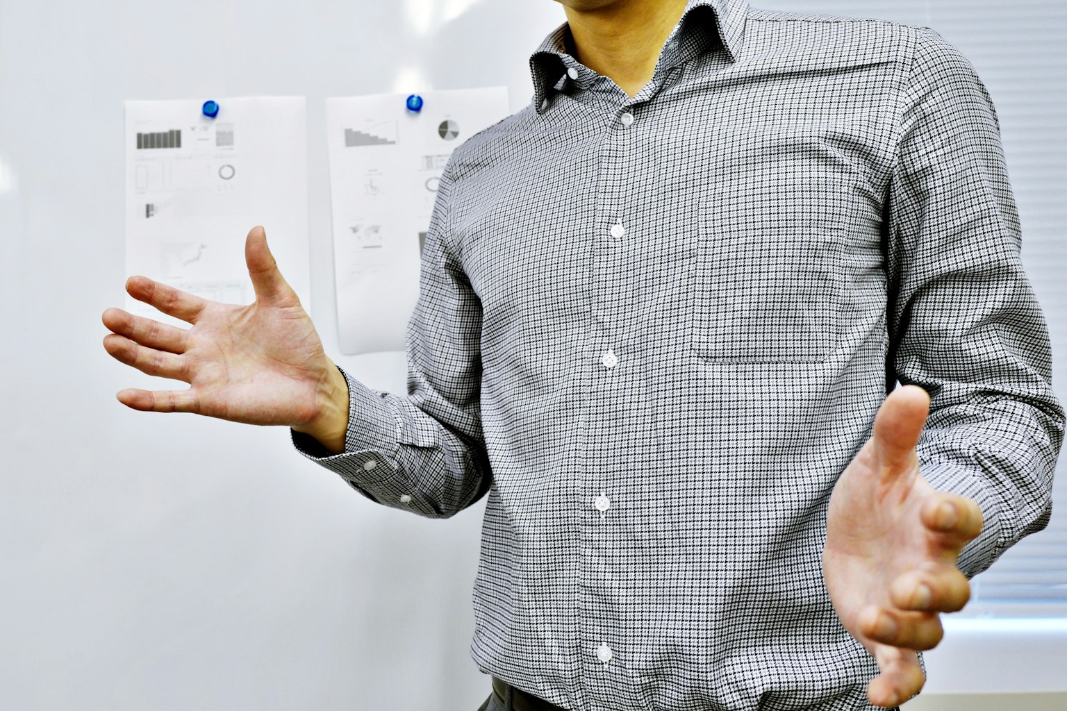 Hombre con camisa a cuadros gesticulando con las manos abiertas con documentos de fondo