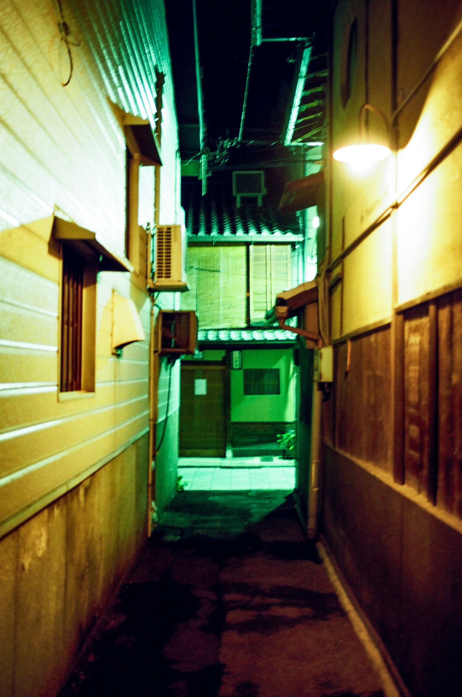 ซอยแคบที่ถูกไฟเขียวส่องสว่างแสดงผนังและประตูบ้าน