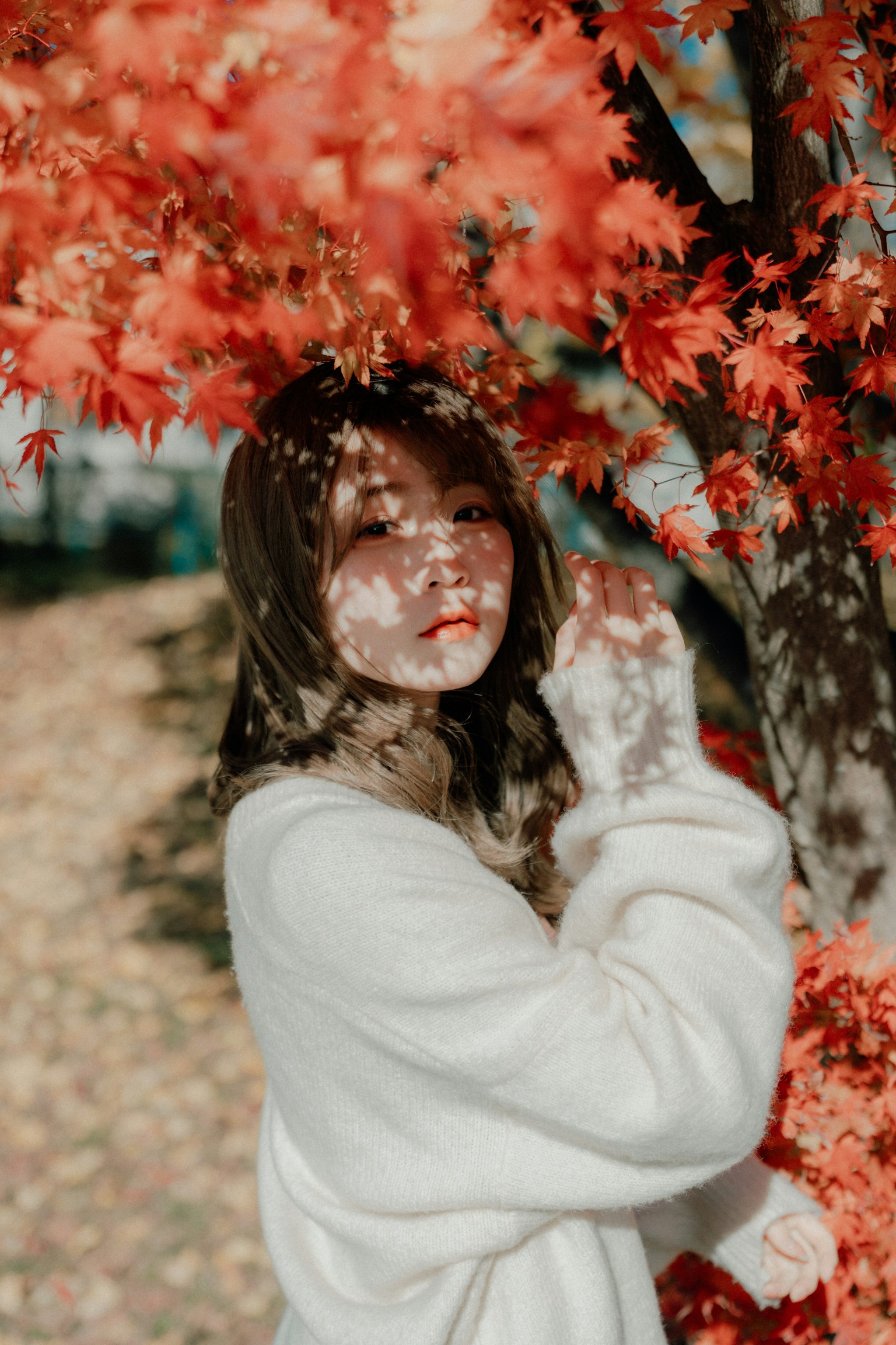 Retrato de una mujer rodeada de hojas rojas que lleva un suéter blanco y sonríe