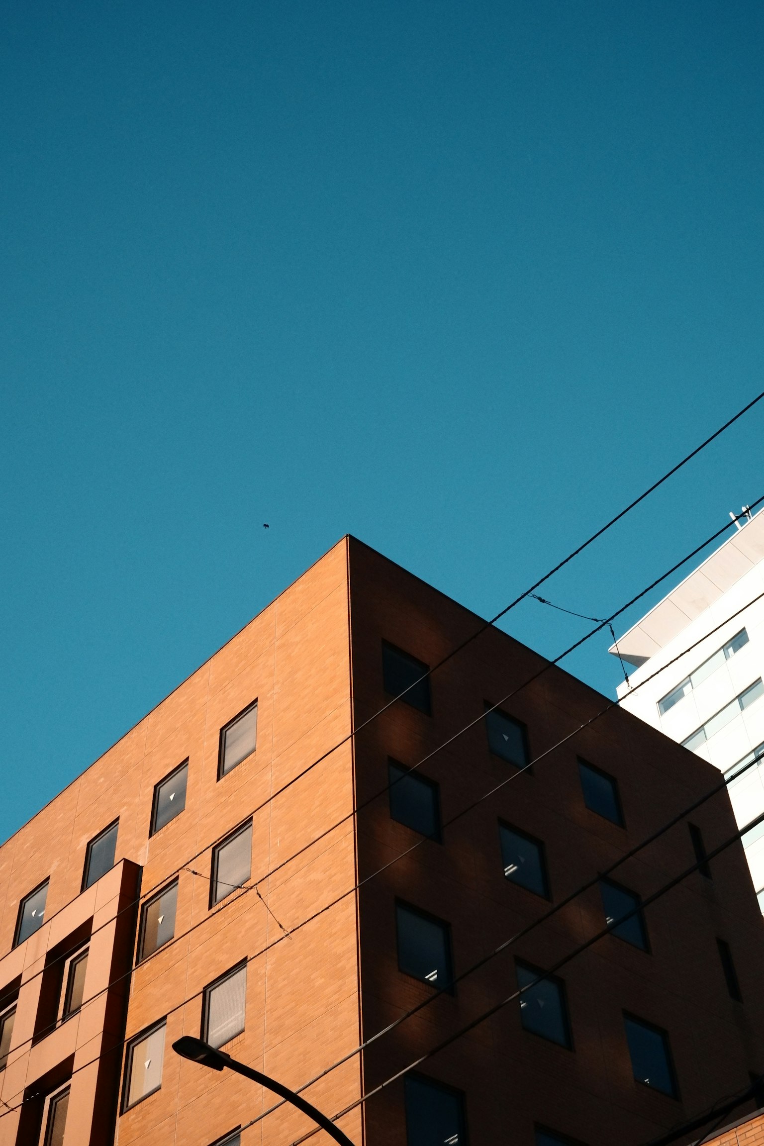 Parte superior de un edificio naranja bajo un cielo azul con un edificio blanco cercano