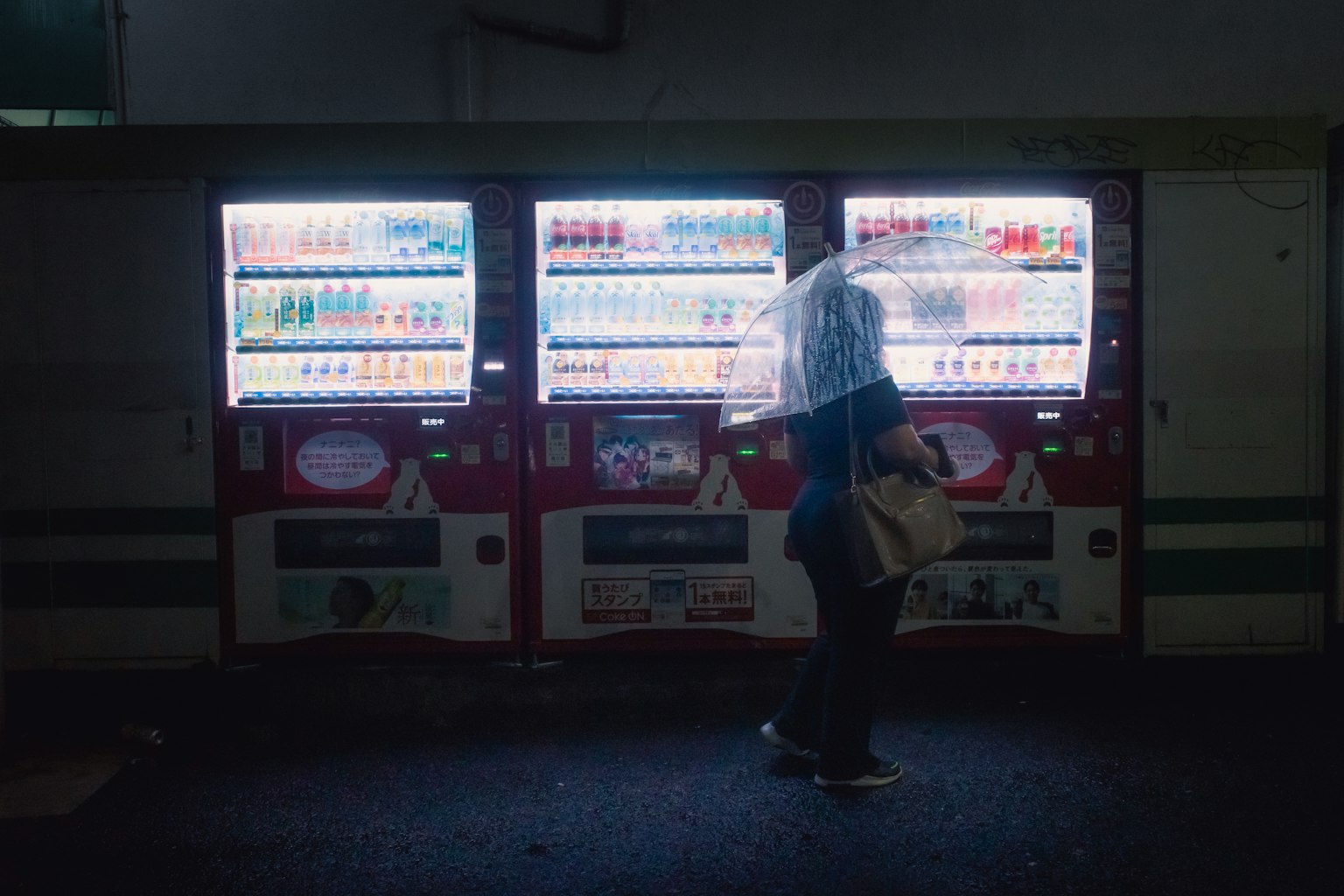 Silhouette di una persona con un ombrello davanti a distributori automatici