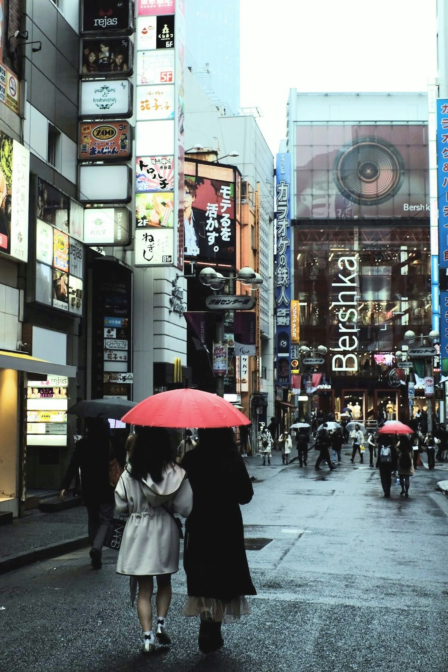 Zwei Frauen gehen im Regen mit einem roten Regenschirm in einer belebten Straße