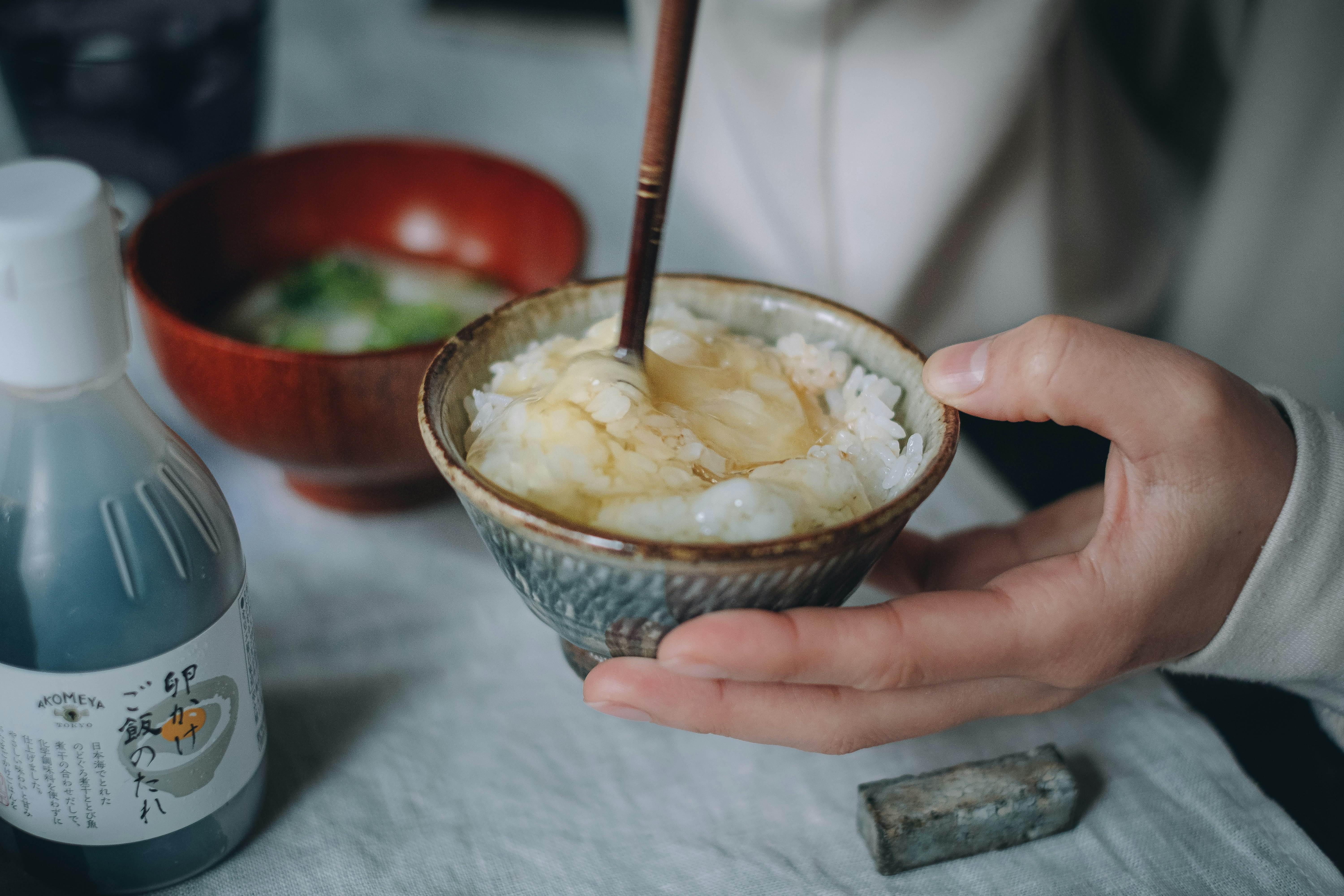 手に持った味噌汁椀に箸でご飯をよそっている食卓