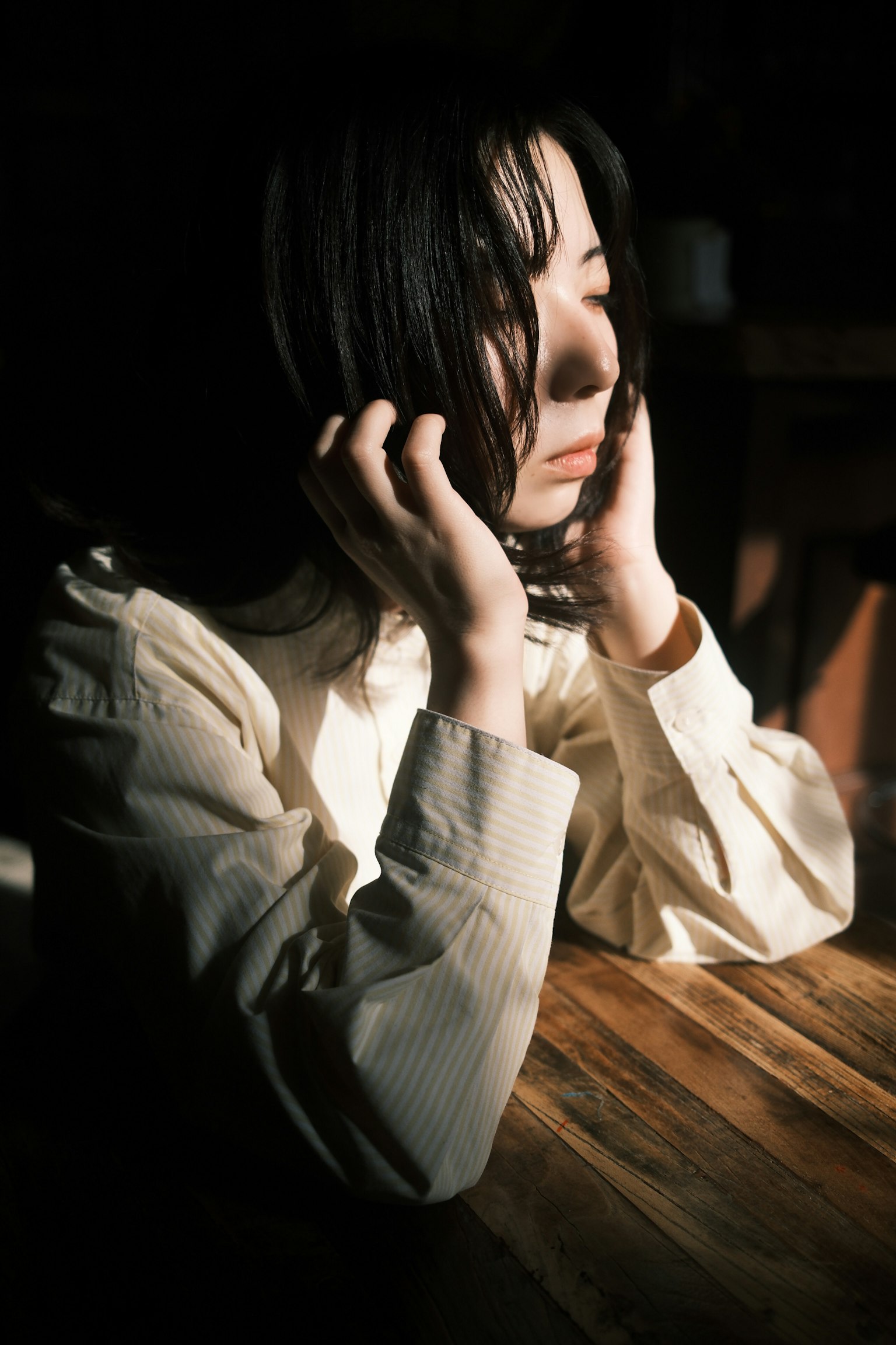 女性が静かに考え込んでいる姿 暗い背景に自然光が当たる