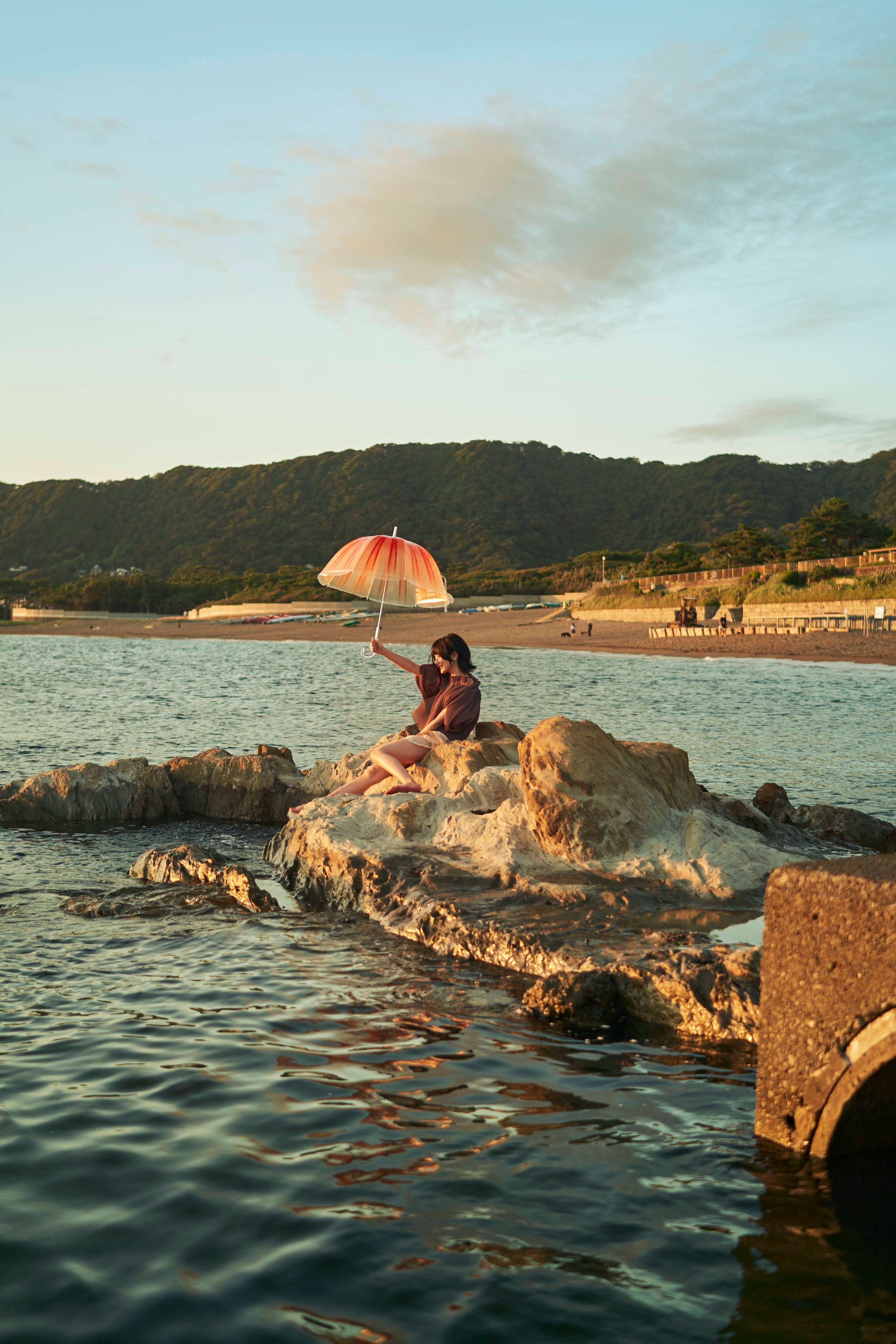 海辺の岩場で日傘をさす人と夕景