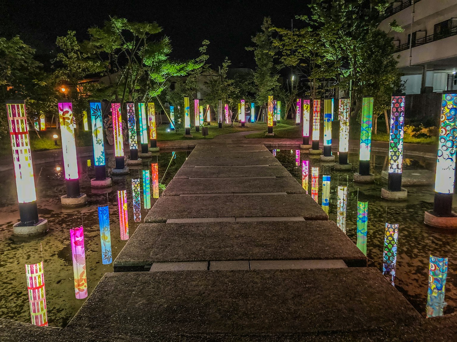 Beleuchtete Säulen, die einen Steinweg in einem Nachtpark säumen