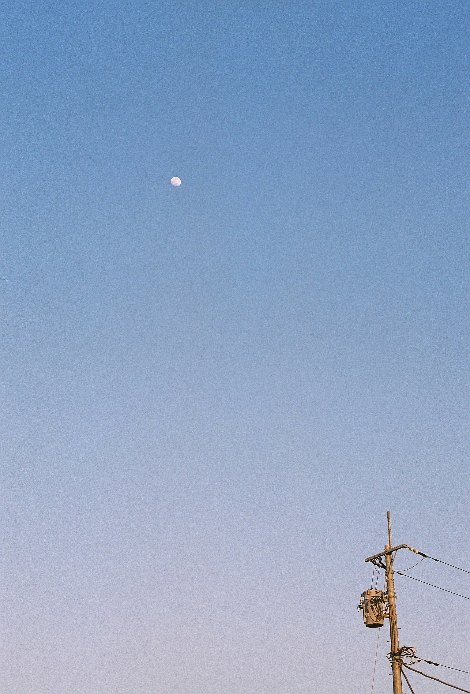 pequeña luna en un cielo azul despejado con poste eléctrico