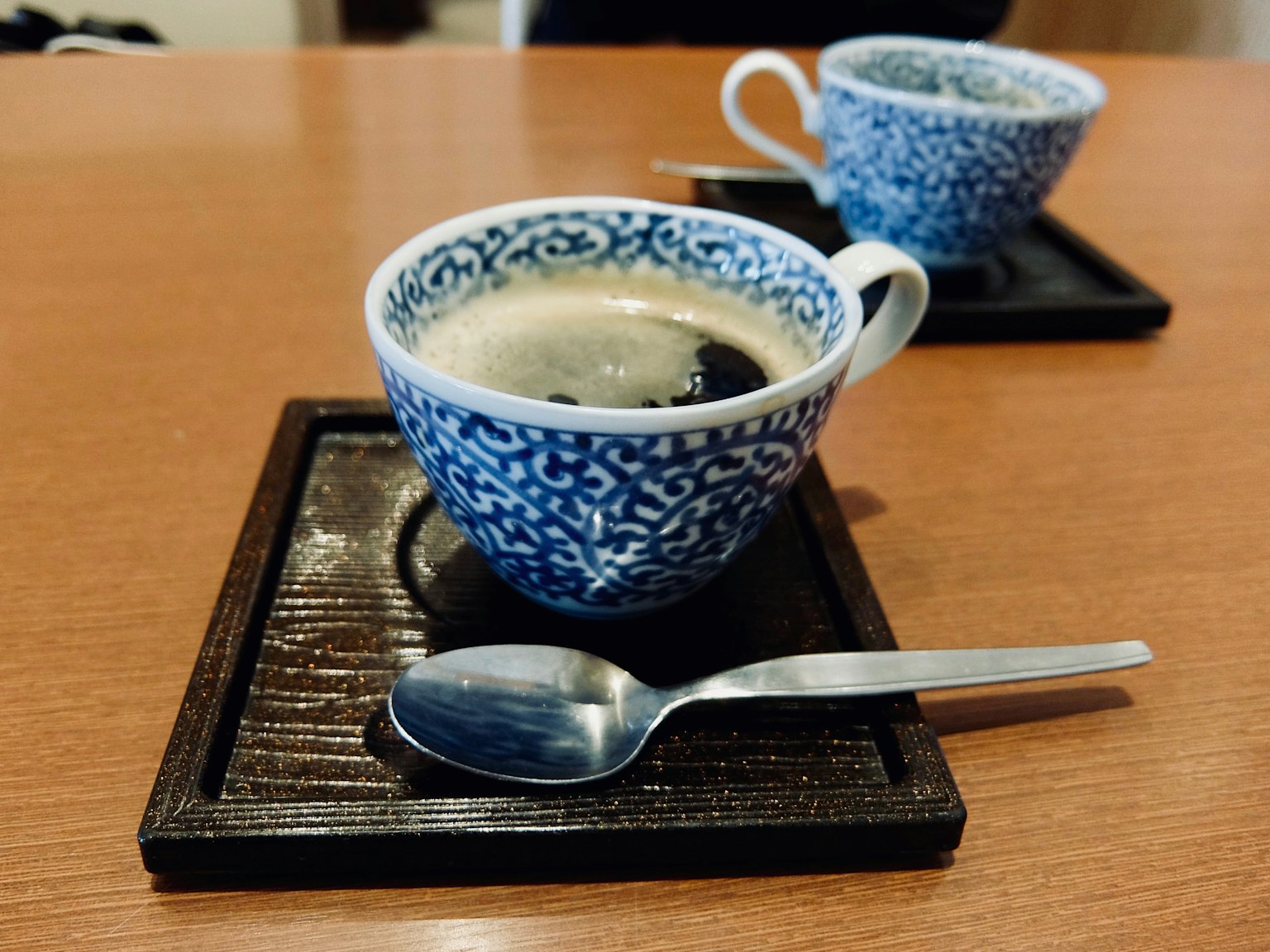 木托盘上的蓝色图案杯中的咖啡和一把勺子