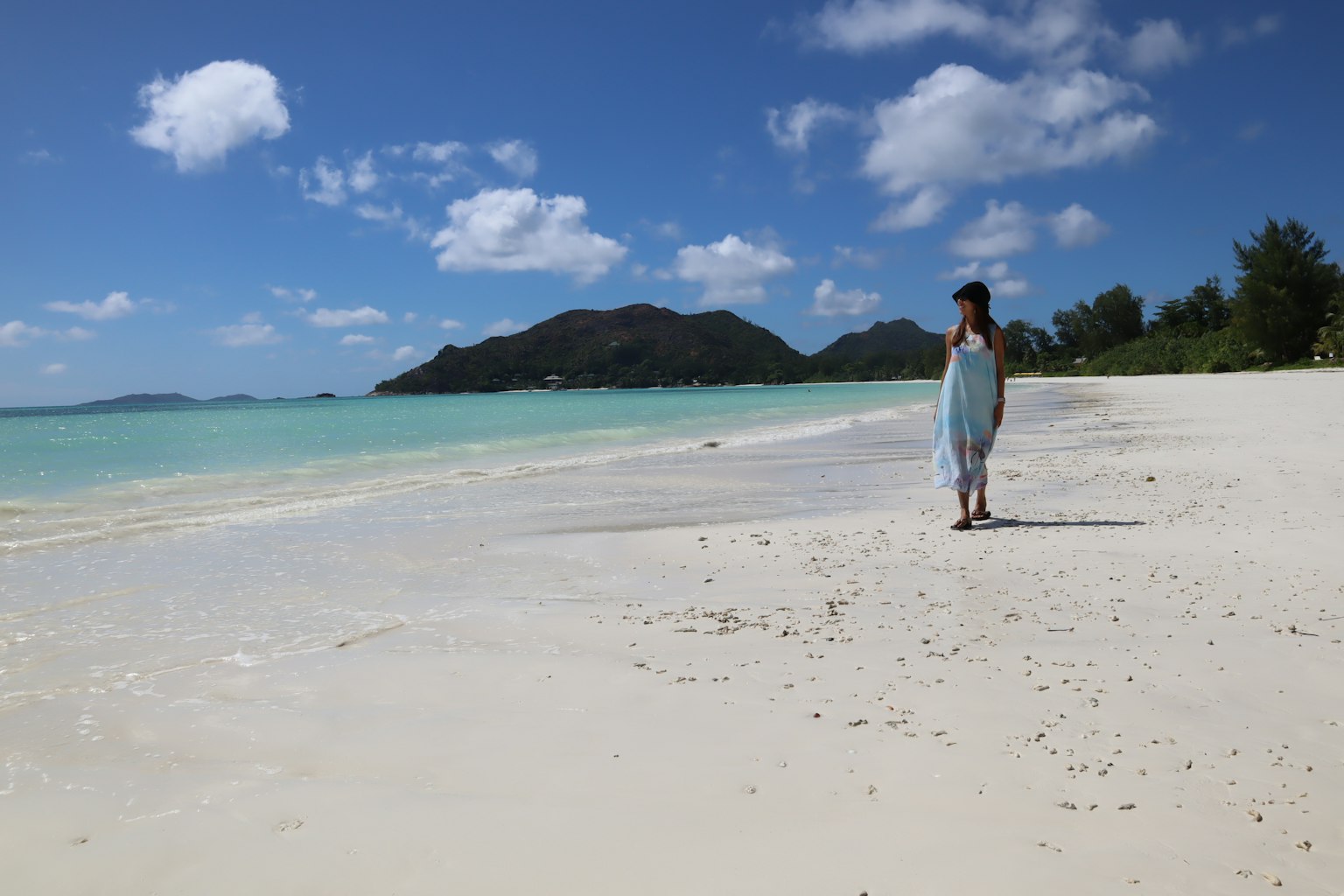 Une femme marchant sur une plage de sable blanc avec de l'eau turquoise et un ciel bleu