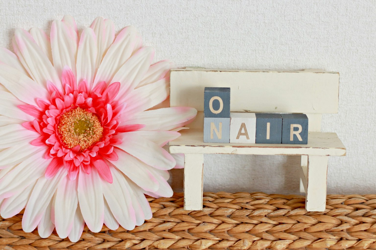 Pequeño banco blanco con letras de bloque que dicen O N A I R y una flor rosa