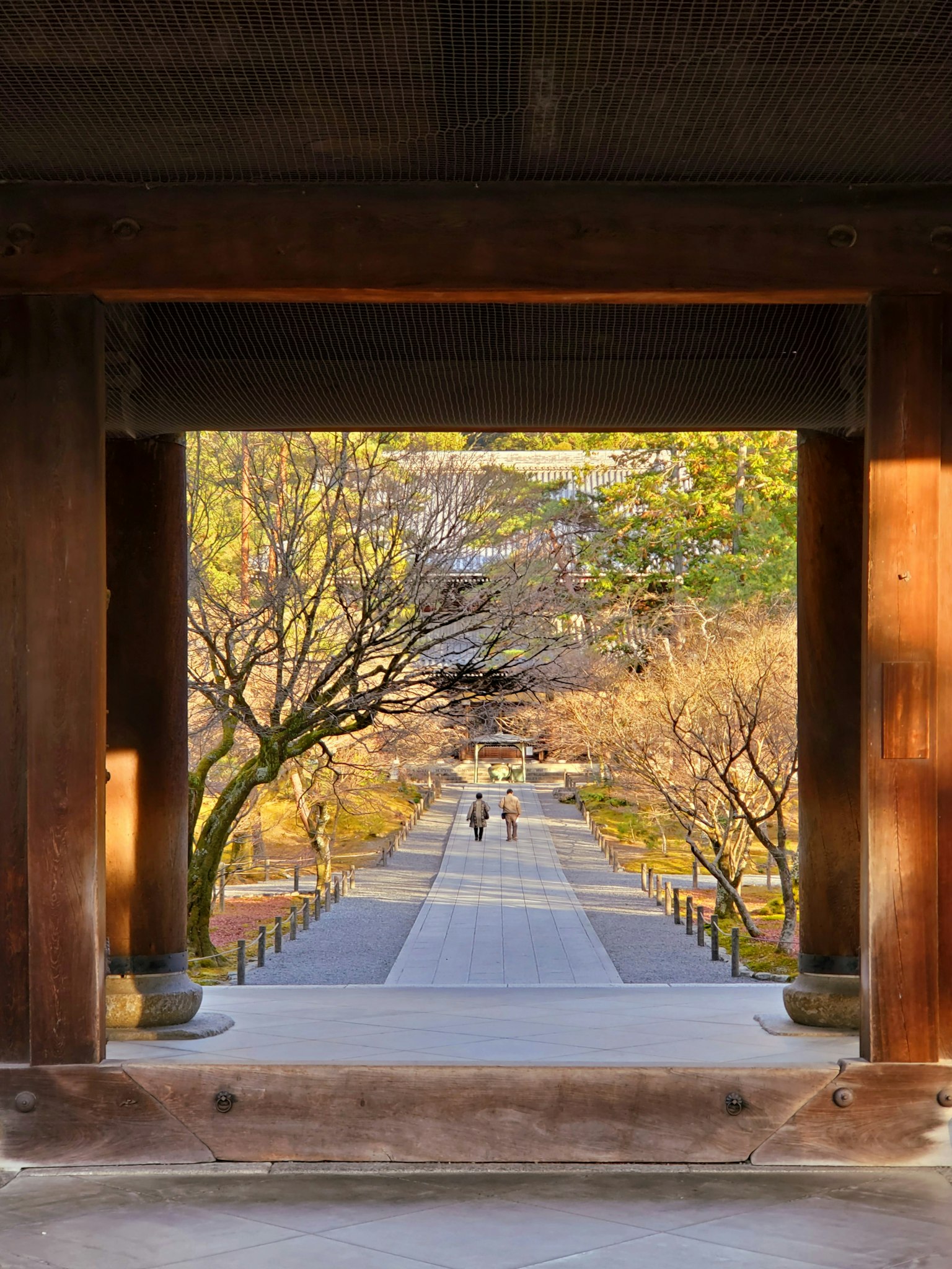 View through a wooden gate of a serene garden pathway with people walking