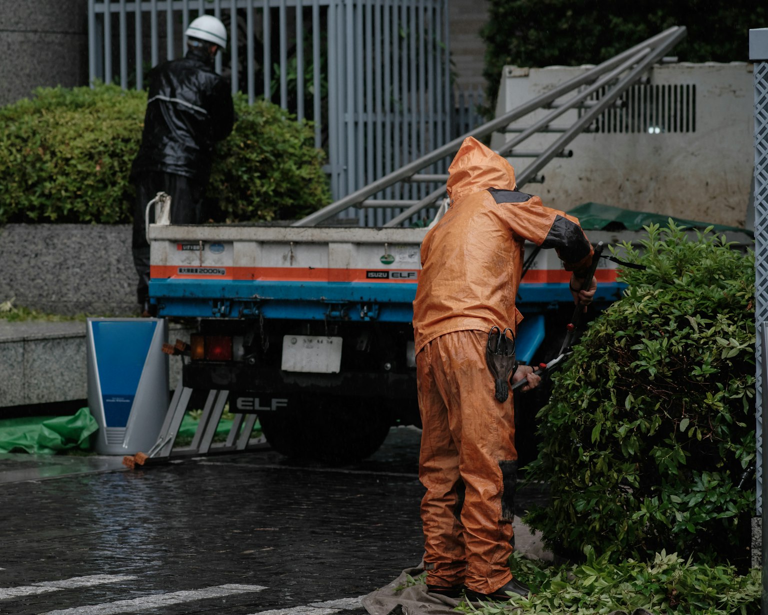 Dos trabajadores con ropa de lluvia junto a un camión bajo la lluvia